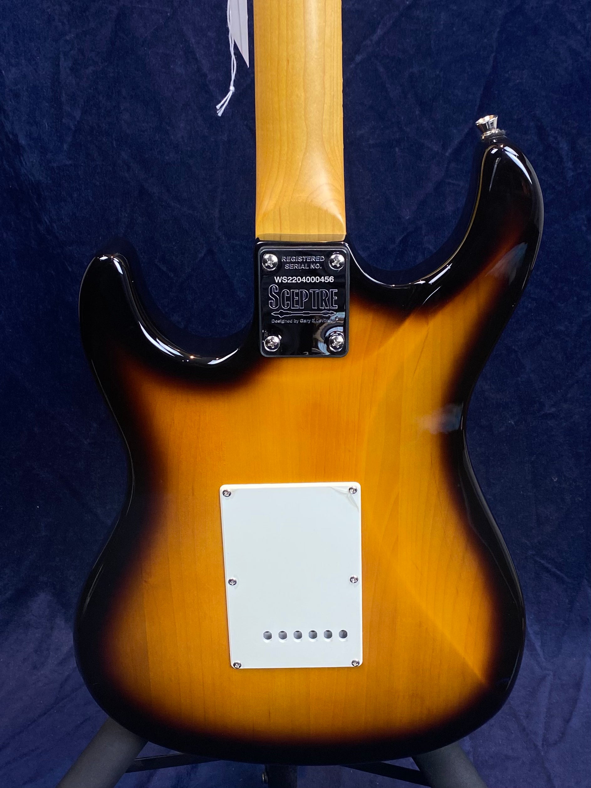Sunburst finish electric guitar back, white rectangular cover plate, neck plate labeled “Sceptre” with serial number, wood grain visible.
