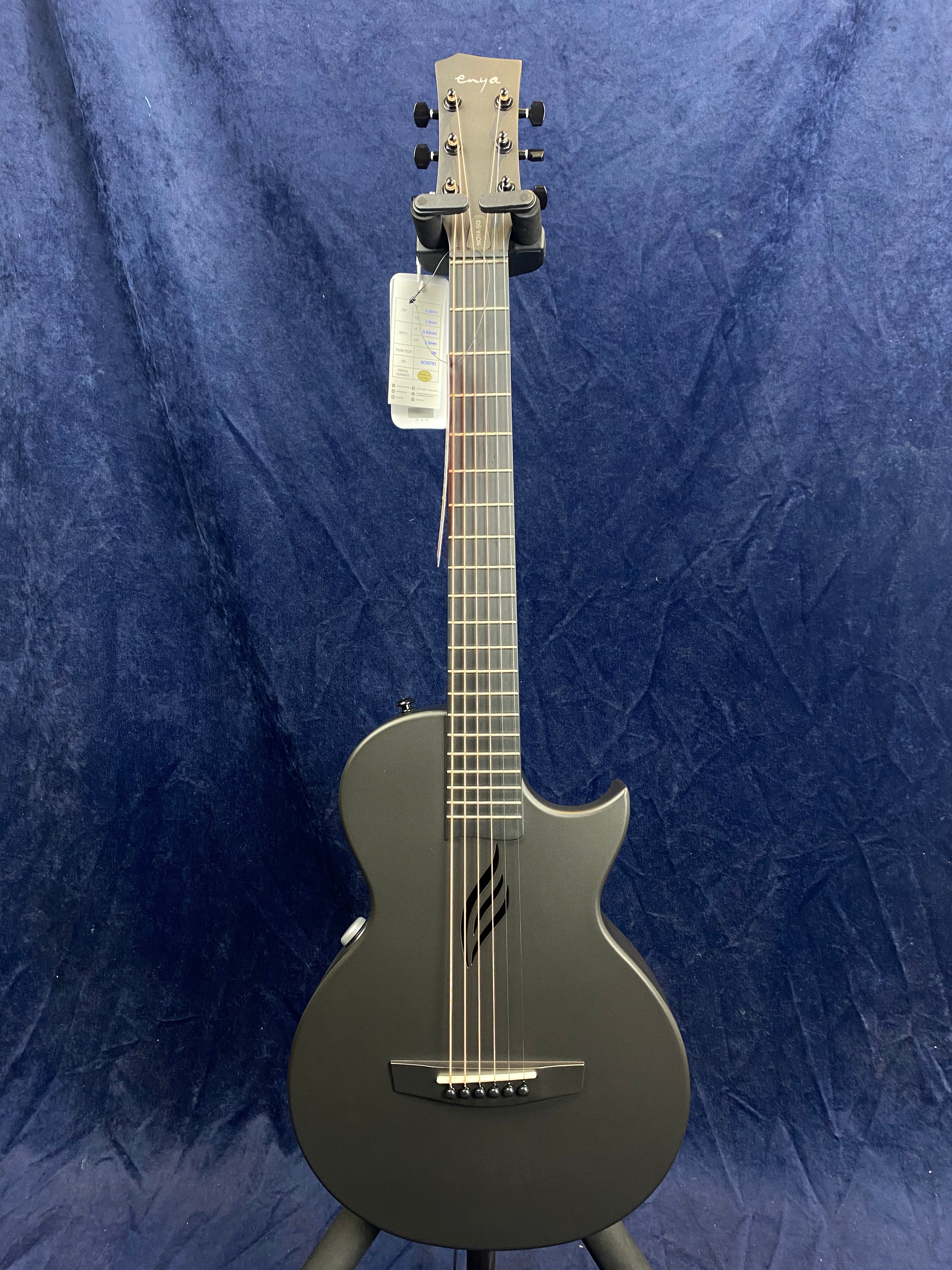 Matte black acoustic guitar with a single cutaway, modern f-hole design, and six strings, displayed upright against a dark blue background.