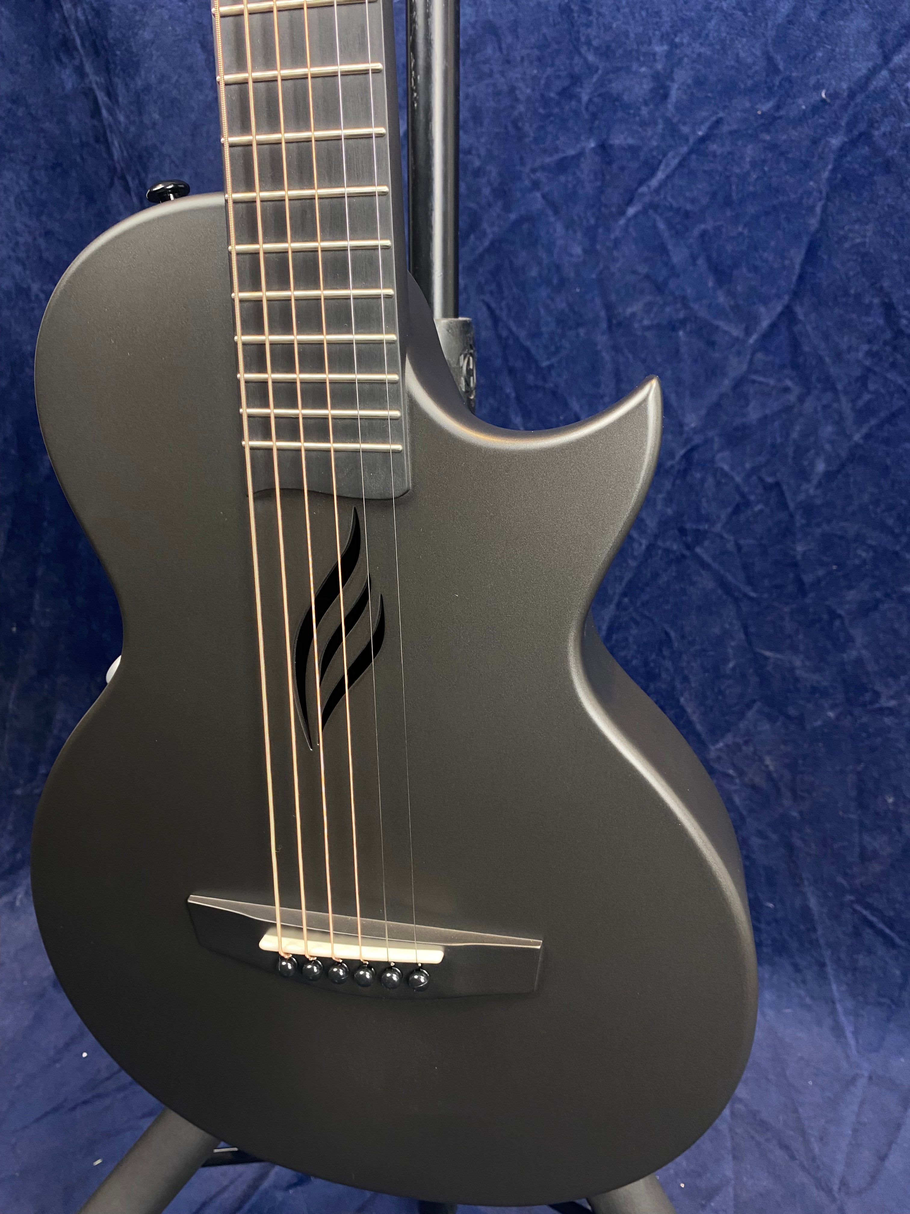 Matte black acoustic guitar with a modern, single-cutaway body and a stylized flame-shaped sound hole instead of a traditional round one.
