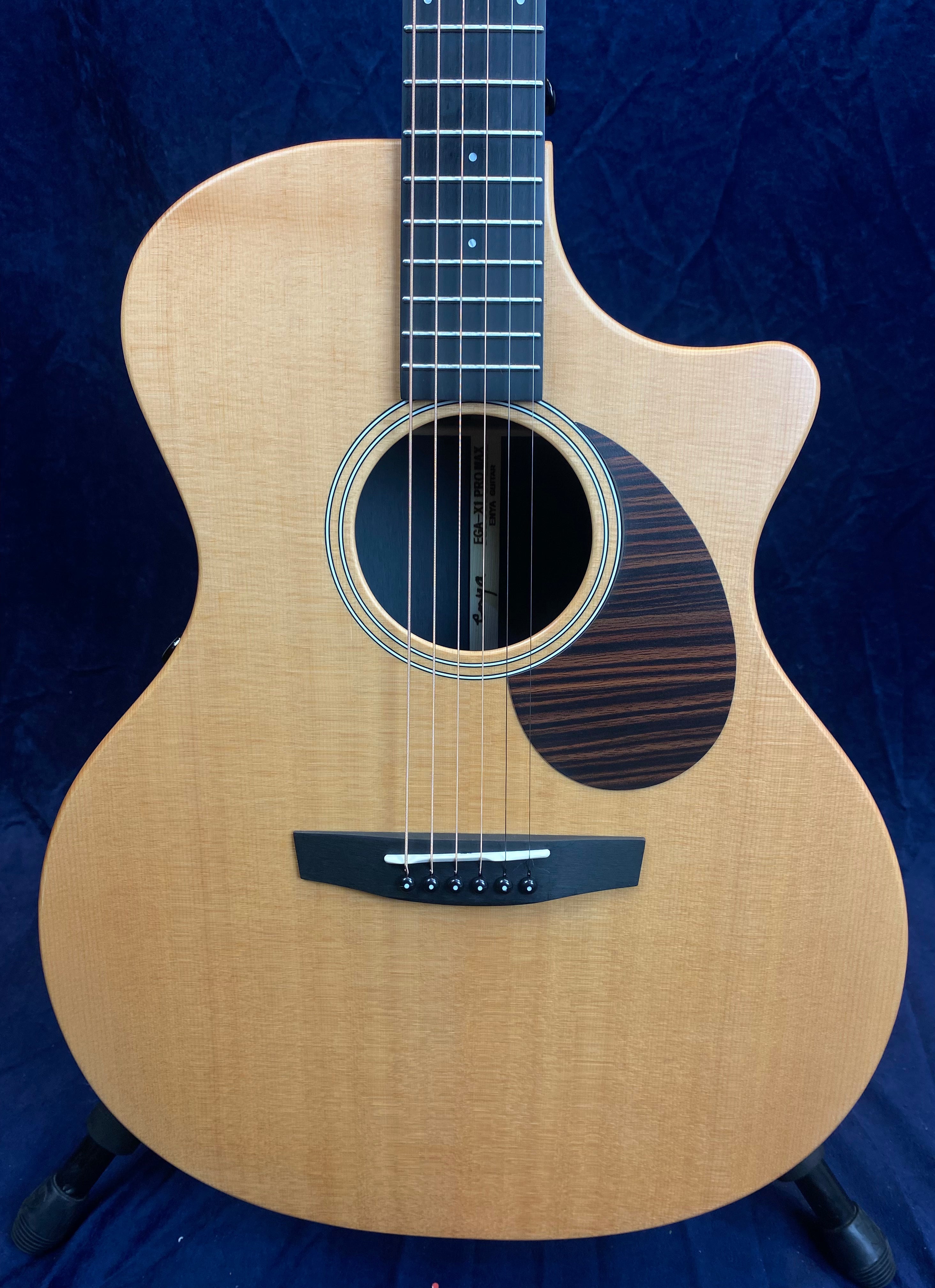 Natural wood acoustic guitar with a single cutaway, dark striped pickguard, six strings, and dark bridge; vertical orientation.