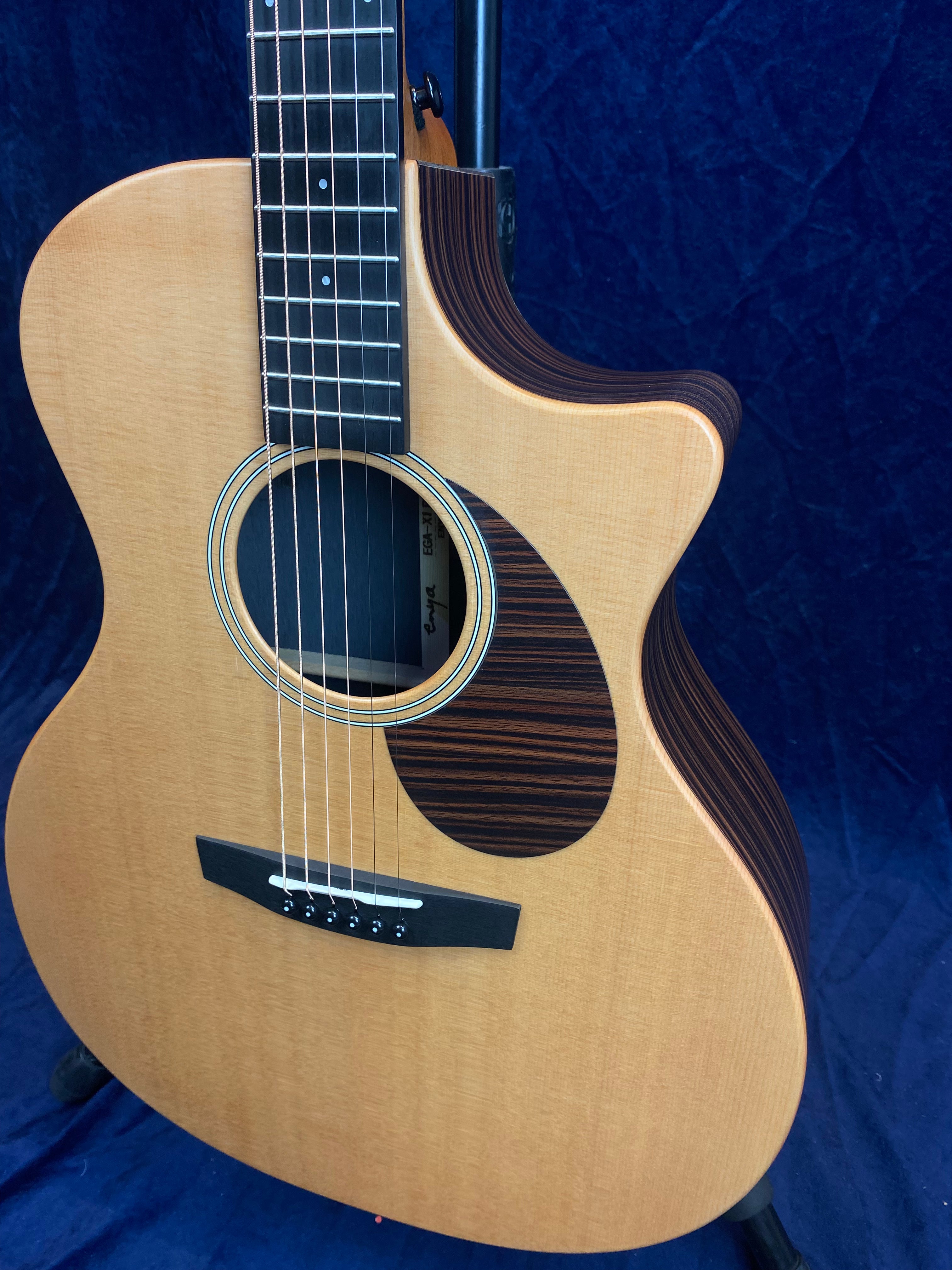 Natural wood acoustic guitar with a cutaway body, striped dark brown pickguard, and matching striped binding on one side.