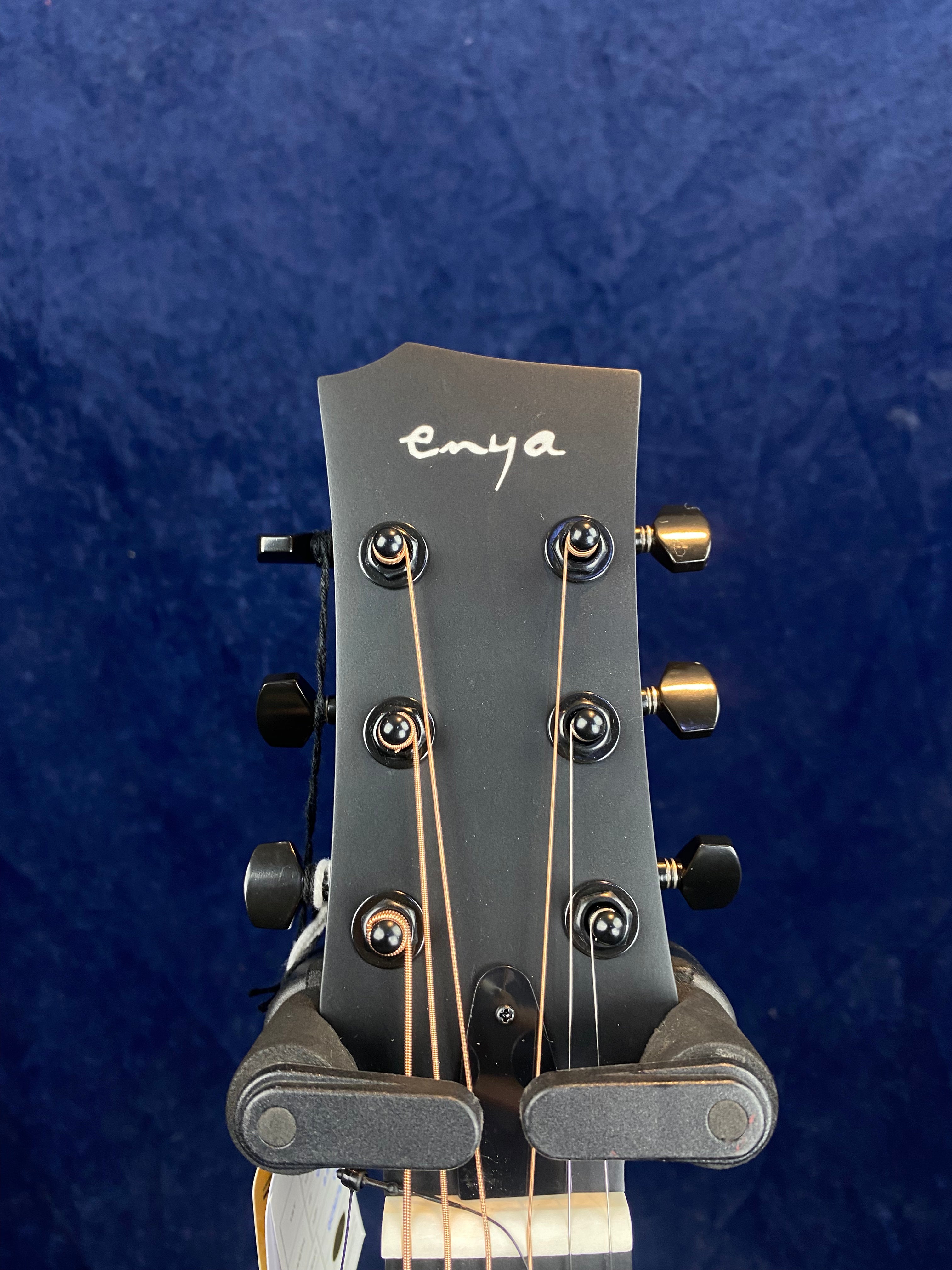 Black acoustic guitar headstock with six tuning pegs, copper and silver strings, and "enya" written in white script at the top.