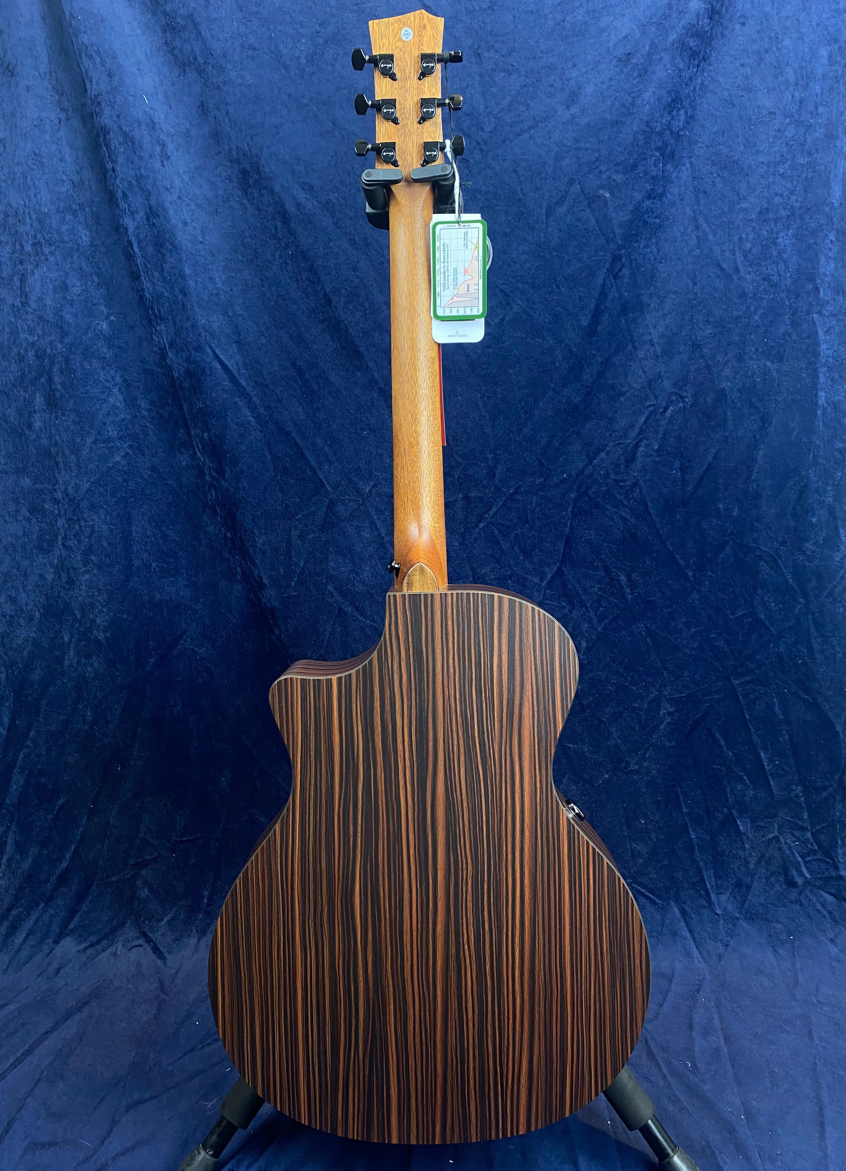 The back of an acoustic guitar with a dark wood finish and vertical light brown stripes, shown upright against a blue fabric background.