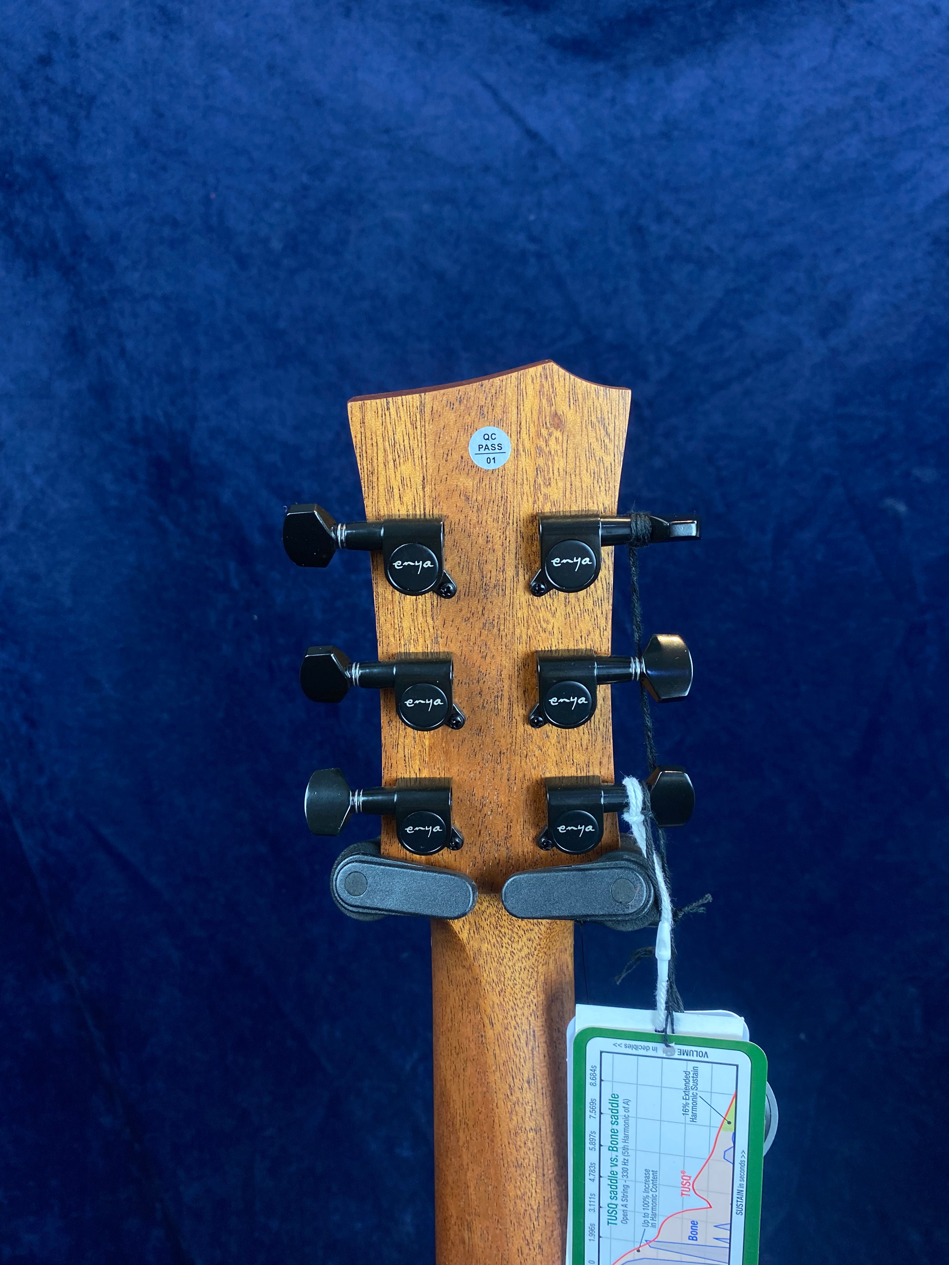 Six black tuning pegs on a wooden acoustic guitar headstock, with "enya" branding and a QC sticker, plus a tag attached with a string.