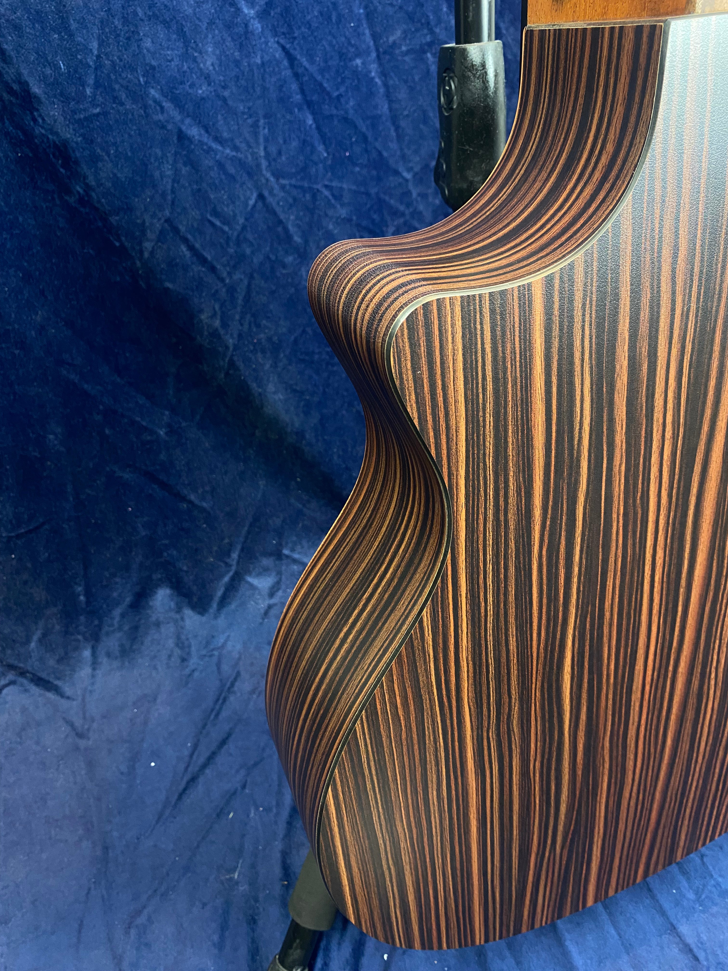 Curved side of an acoustic guitar with a dark wood body featuring striking, vertical orange and brown stripes against a dark blue background.