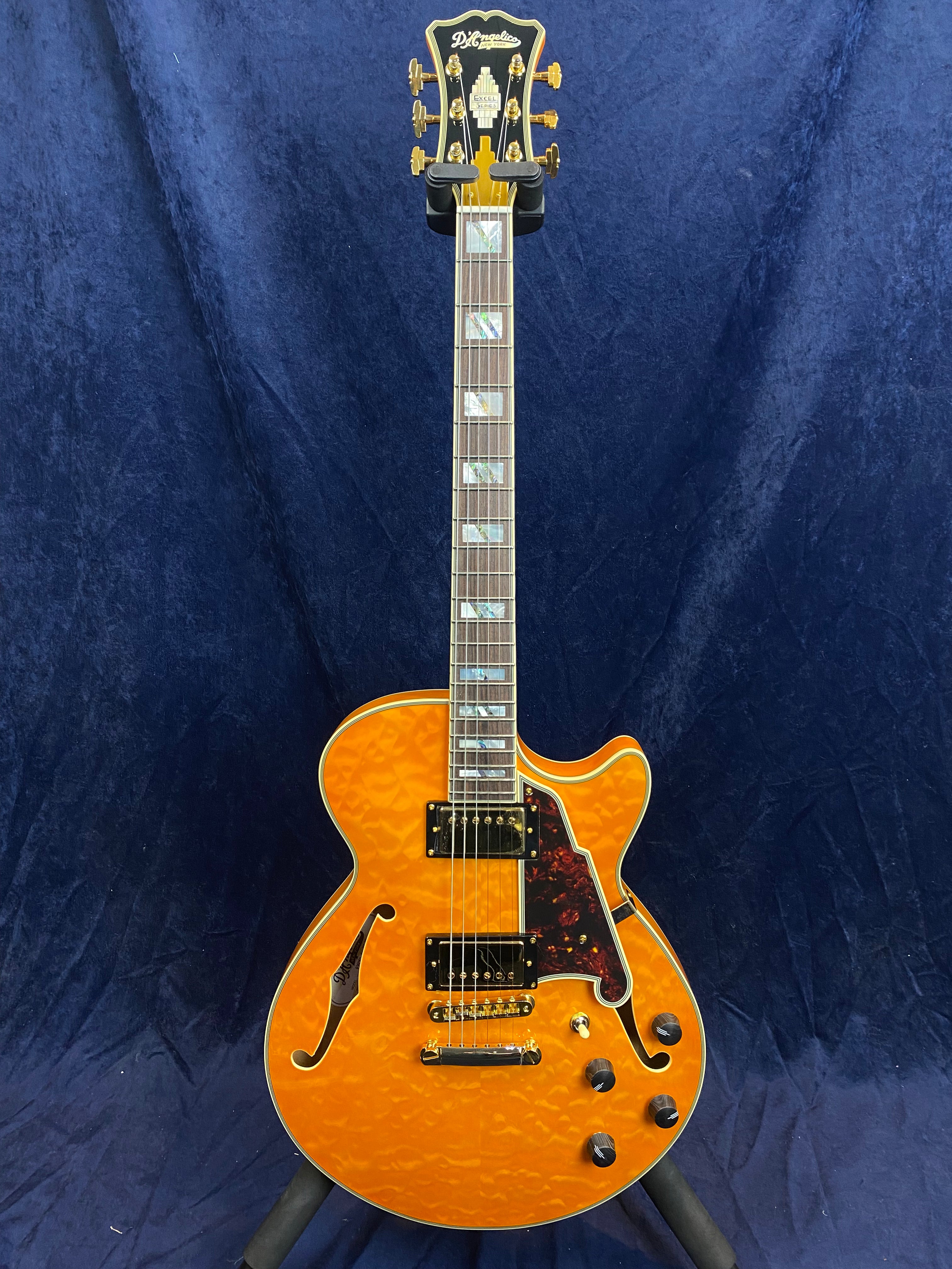 Orange semi-hollow electric guitar with gold hardware, two humbucker pickups, tortoiseshell pickguard, and block inlays on the fretboard.