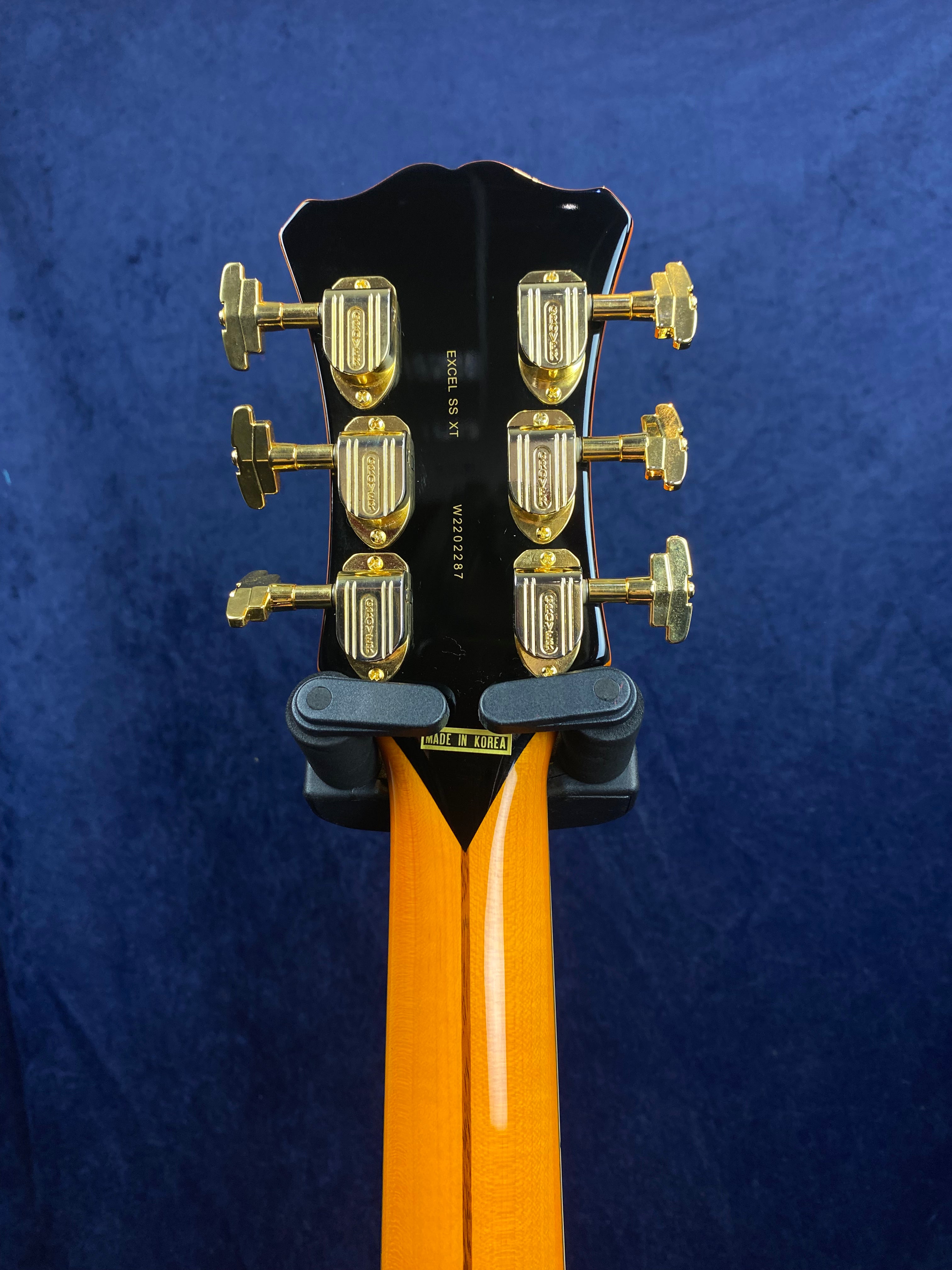 Back of an electric guitar headstock showing six gold tuning pegs, Excel SS XT model marking, and a "Made in Korea" label on a wooden neck.