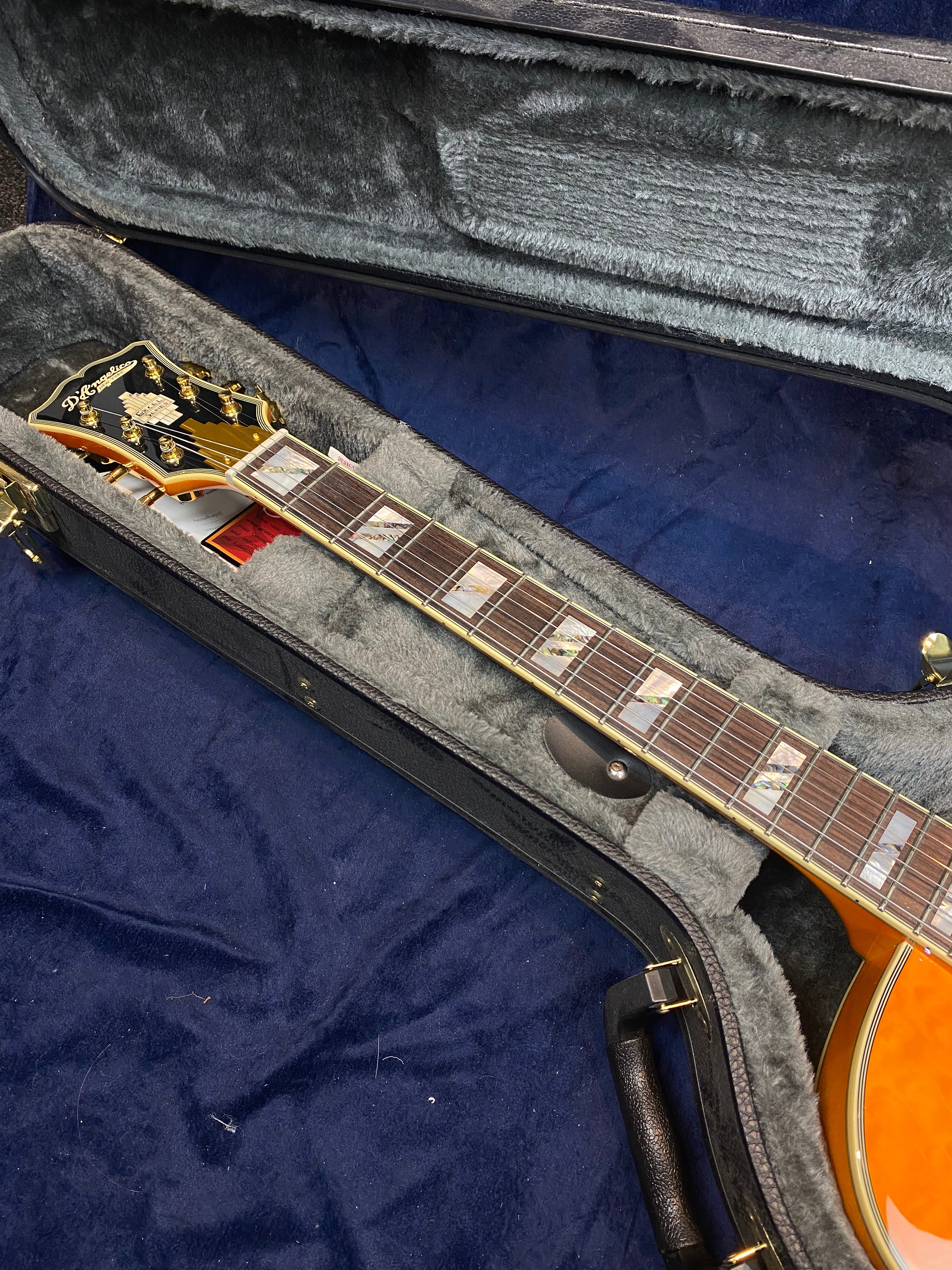 Electric guitar with gold hardware and decorated fretboard rests inside a plush, padded hard case lined with gray fur-like material.