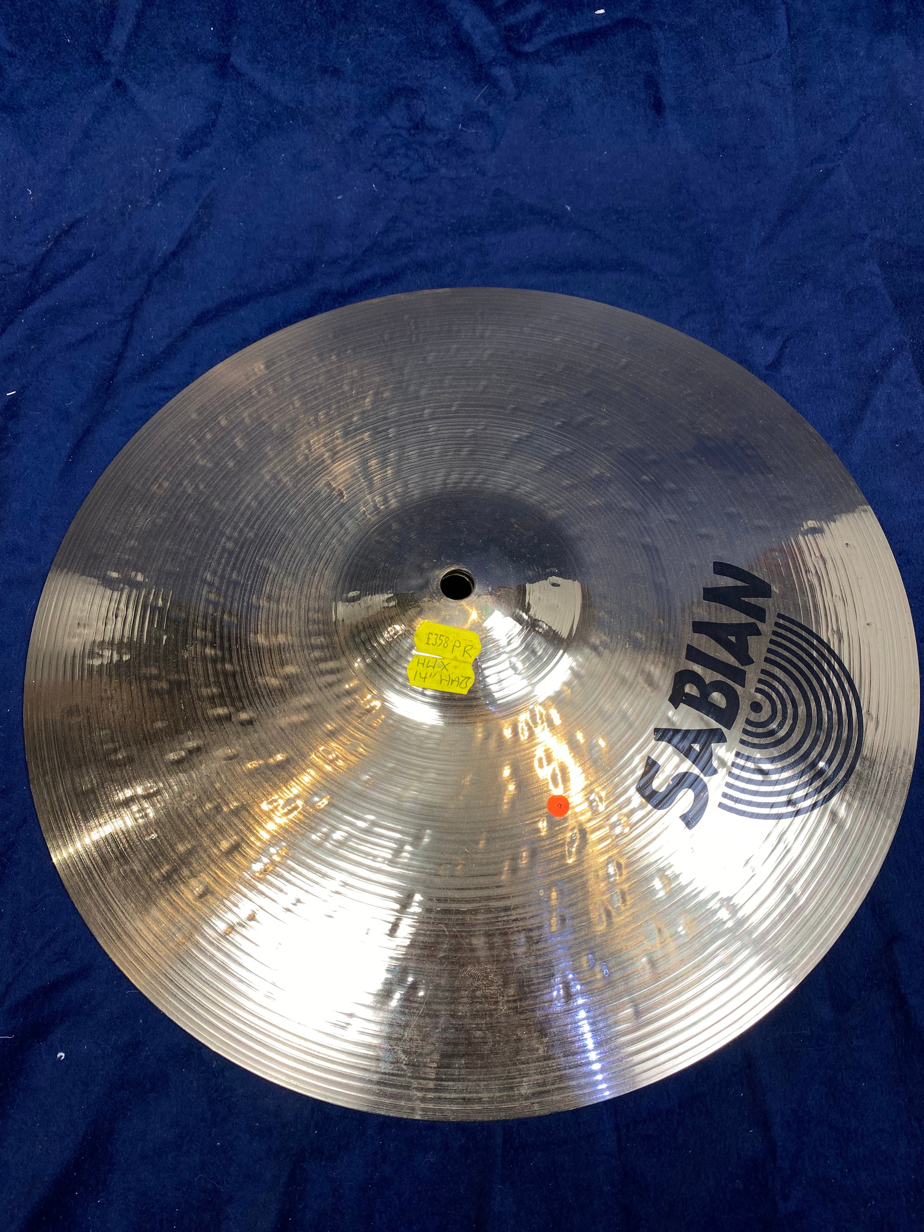 Shiny, metallic Sabian cymbal with concentric circular grooves, a central hole, and yellow sticker labeled "E358 PR HHX 14" HATB".
