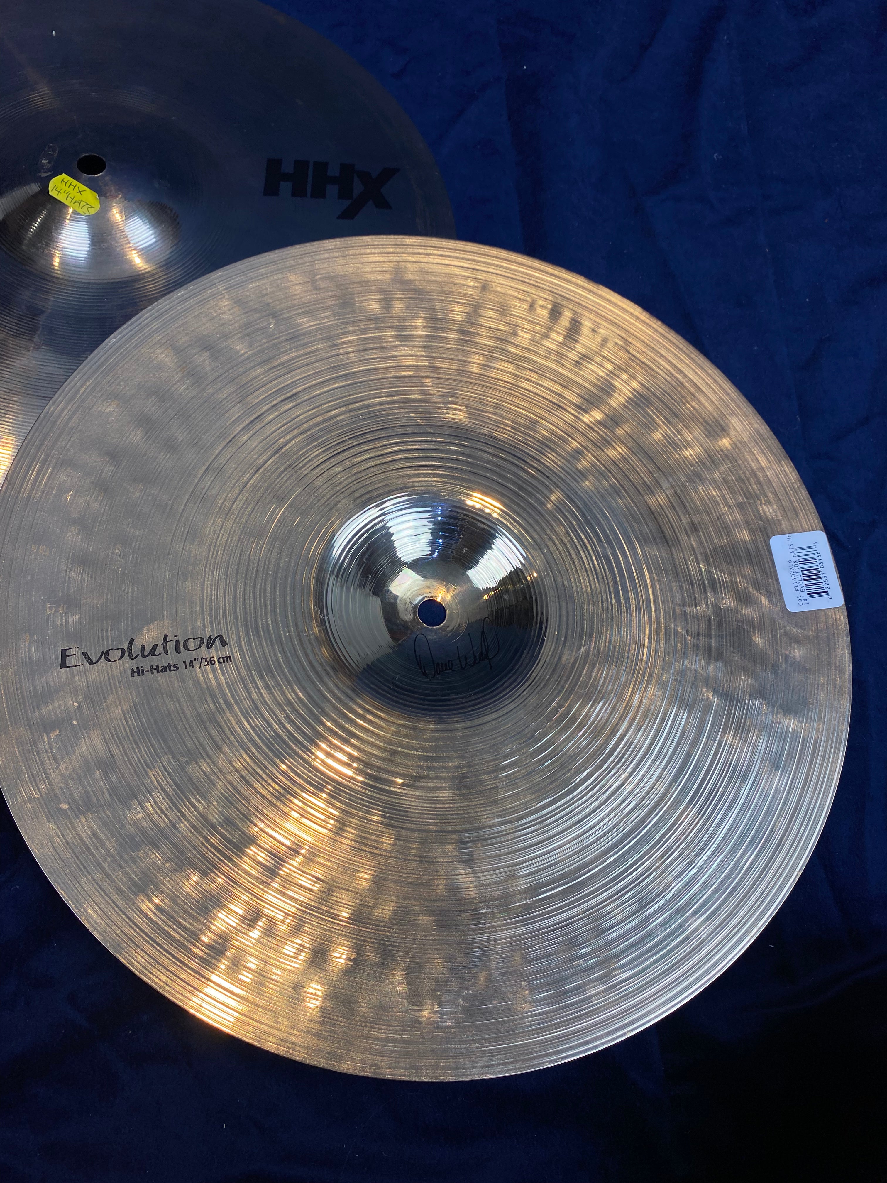 Two shiny metal hi-hat cymbals for drums, one labeled “Evolution Hi-Hats 14” with a barcode sticker, the other partially visible with “HHX” text.