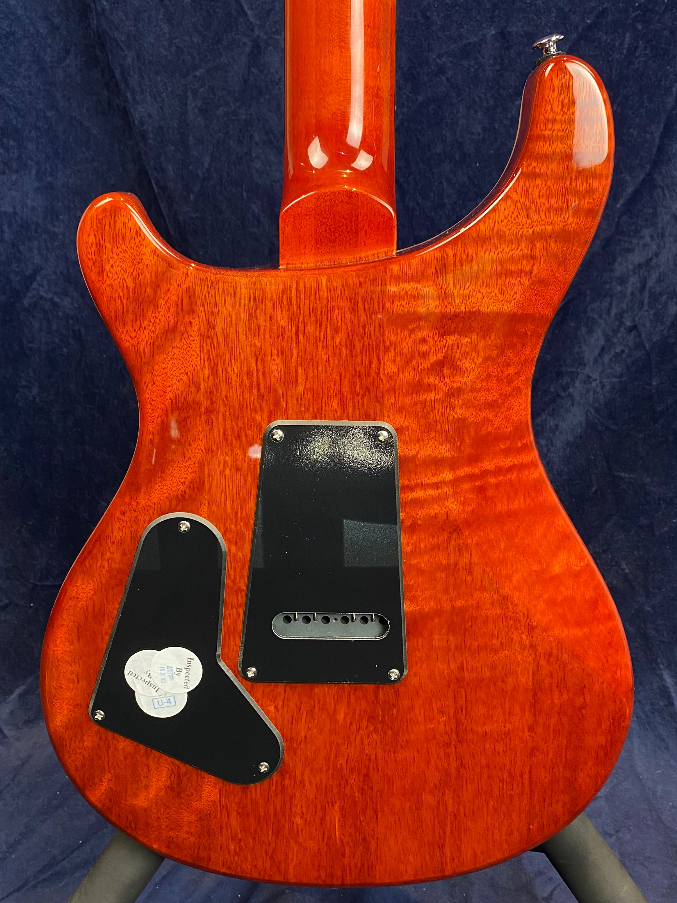 Glossy orange electric guitar back with two black plastic plates and visible wood grain, set against a dark background.