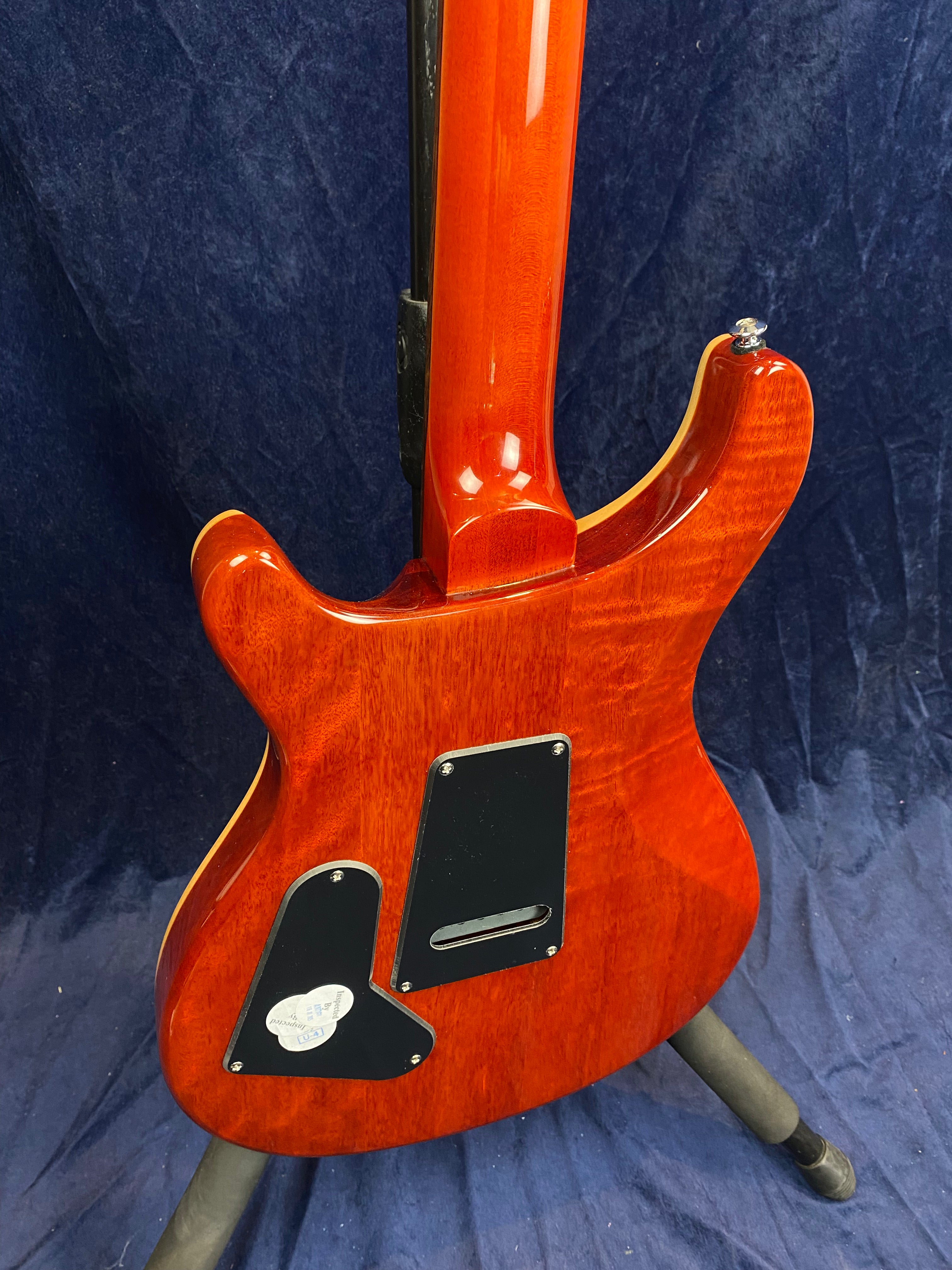 Electric guitar with a glossy red wood finish, two black plastic access panels on the back, and a rounded double-cutaway body shape.