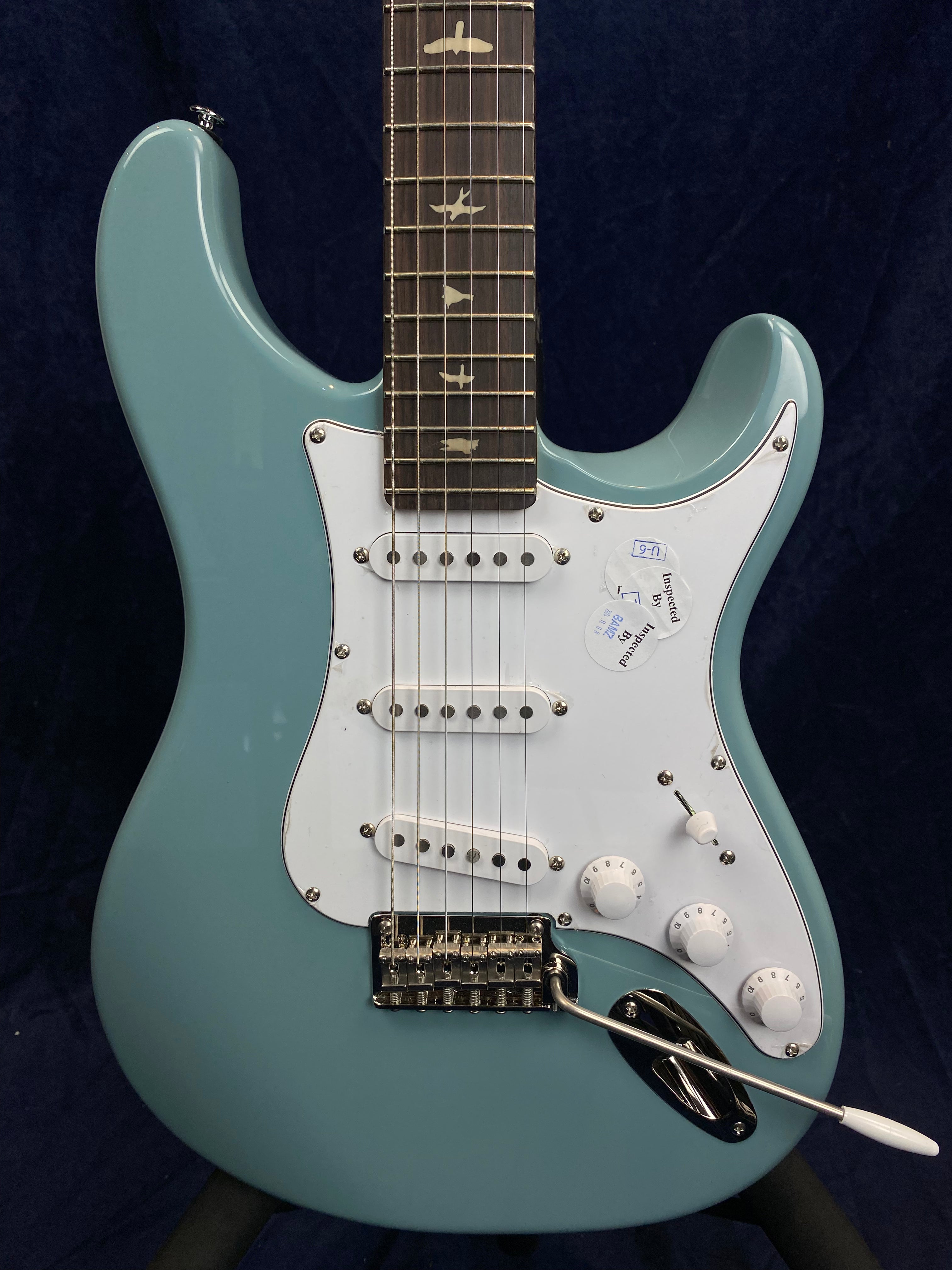 Light blue electric guitar with white pickguard, three single-coil pickups, a tremolo bar, and bird inlays on a rosewood fretboard.