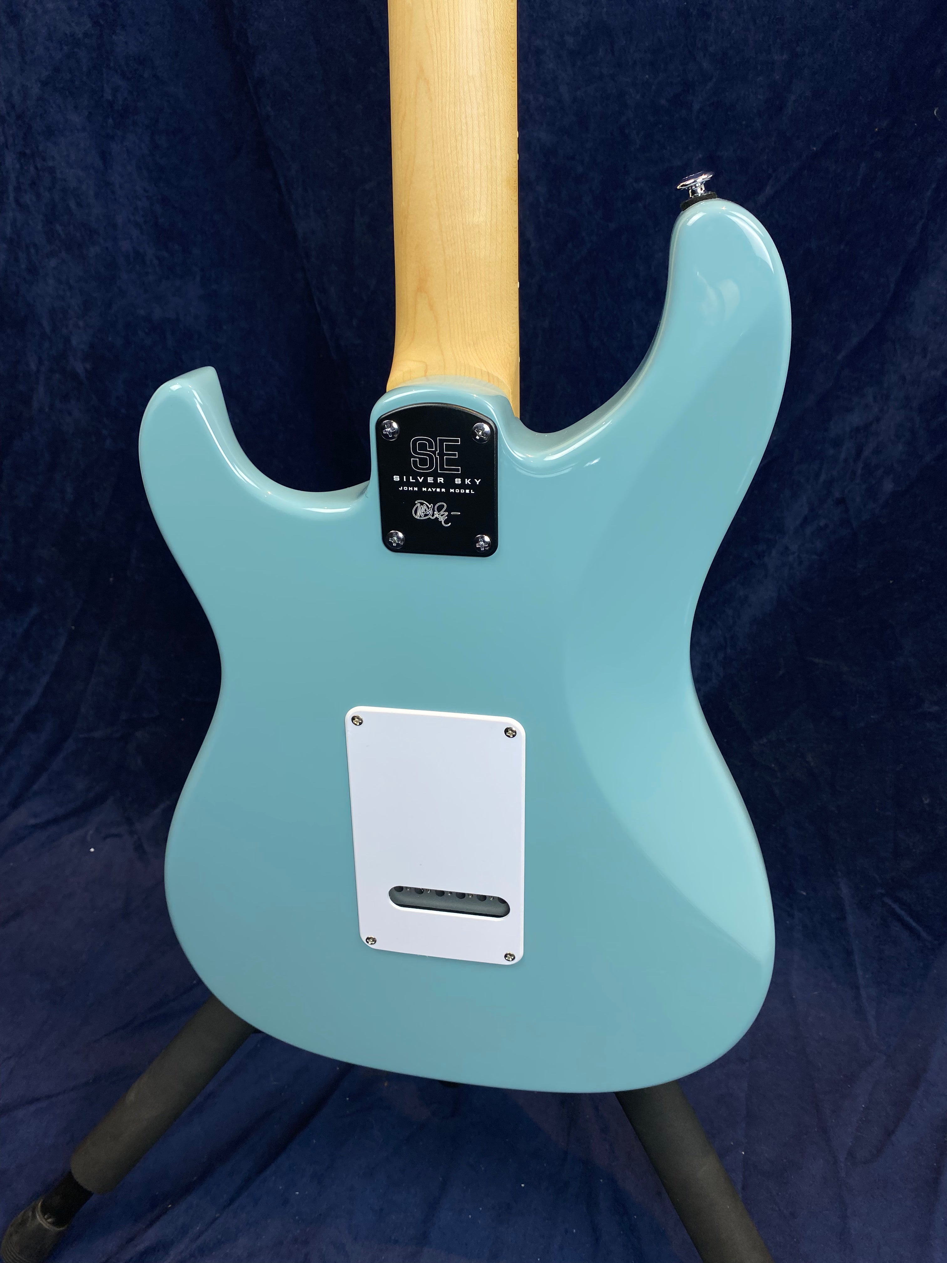 Light blue electric guitar seen from the back, with a natural wood neck and a white electronic cavity cover on the body.