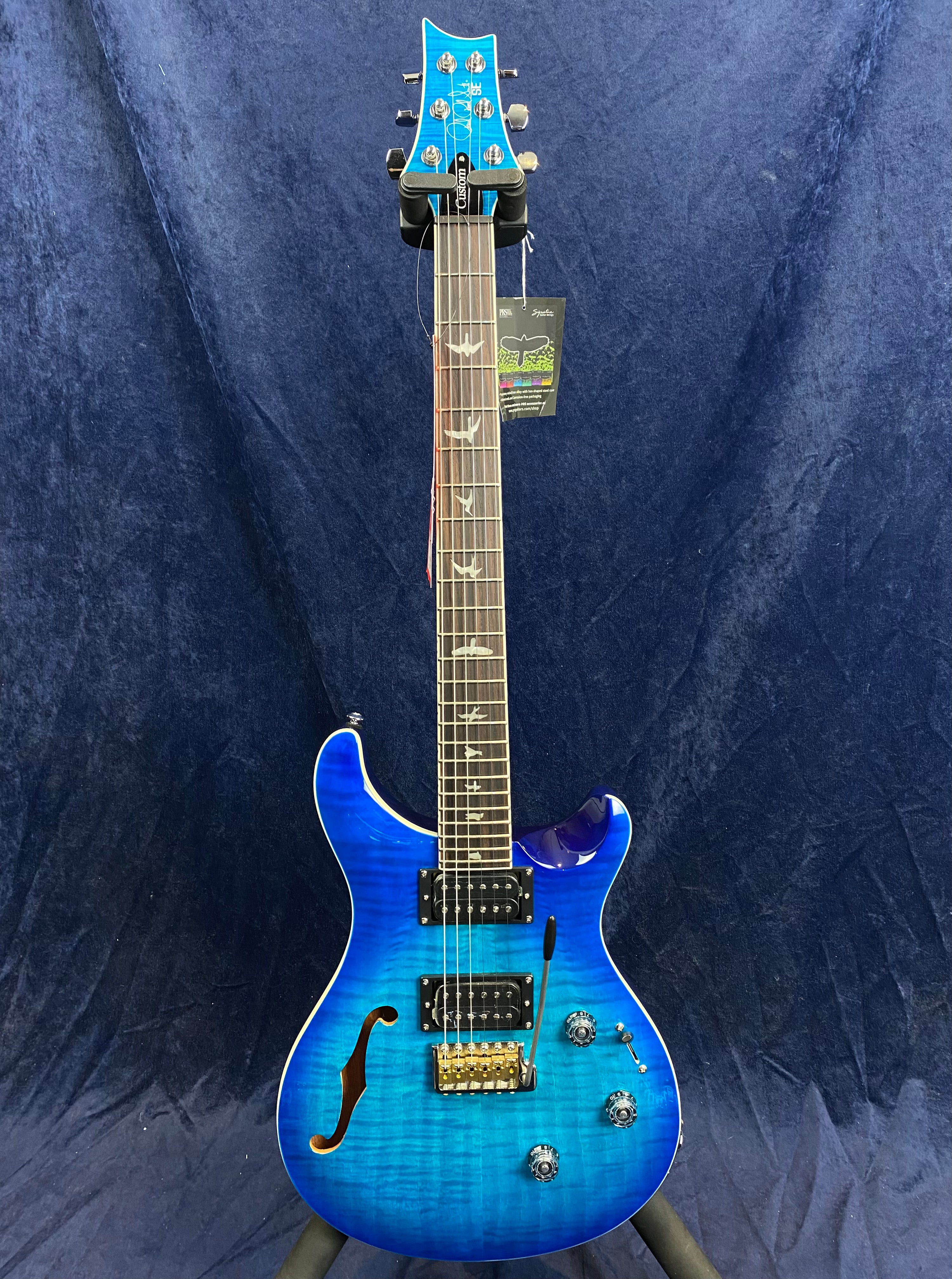 Blue electric guitar with a semi-hollow body, two humbucker pickups, gold bridge, and bird inlays on the fretboard.