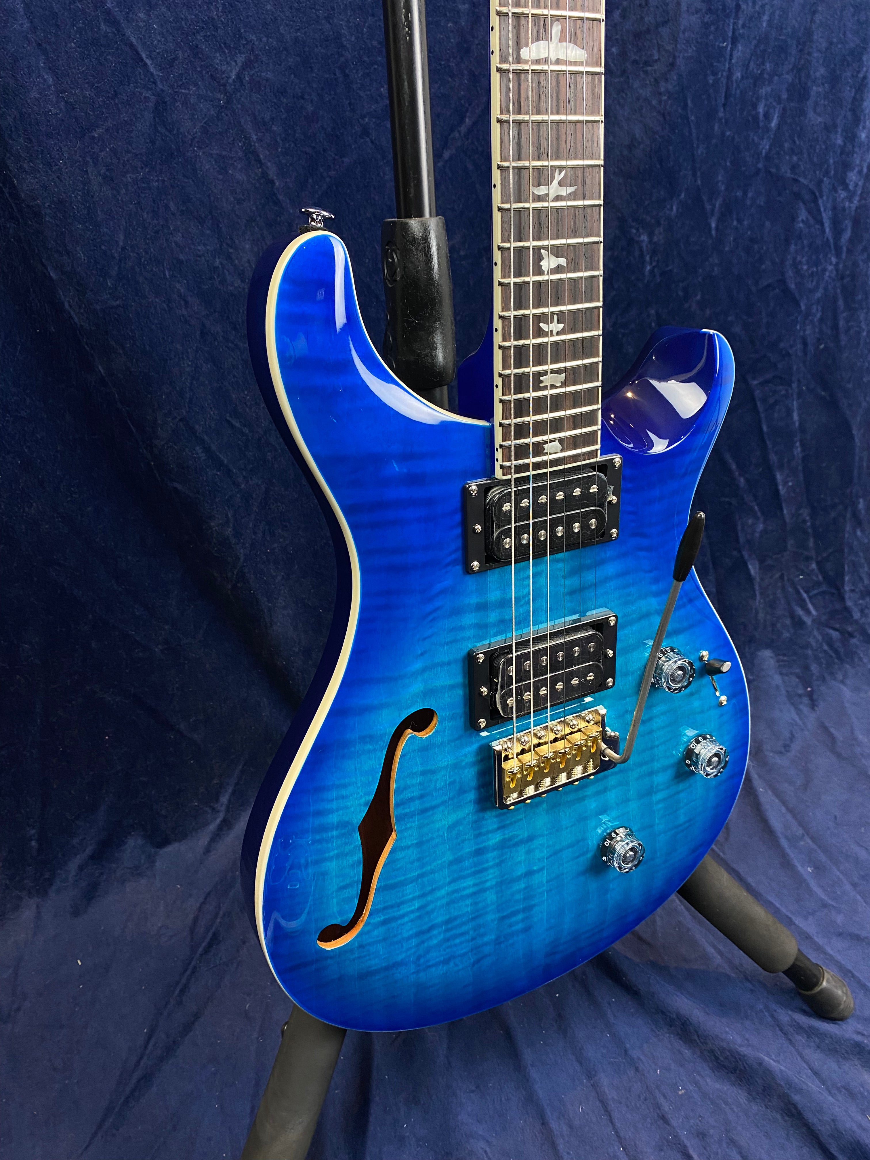 Blue electric guitar with a semi-hollow body, f-hole, two humbucker pickups, three control knobs, gold bridge, and bird inlays on the rosewood fretboard.