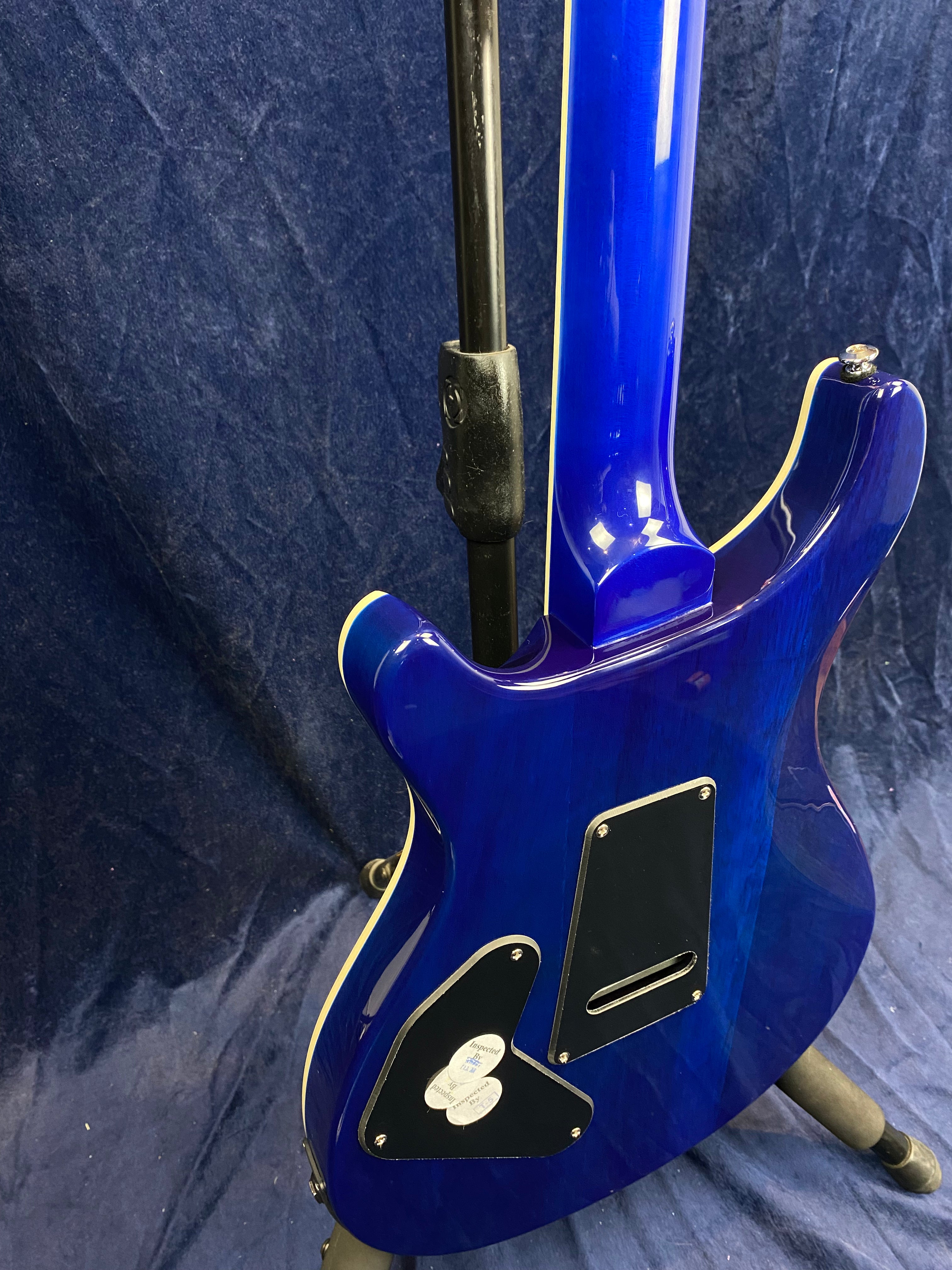 Electric guitar with a glossy blue finish viewed from the back, showing two black rear cavity plates and light trim on the body and neck.