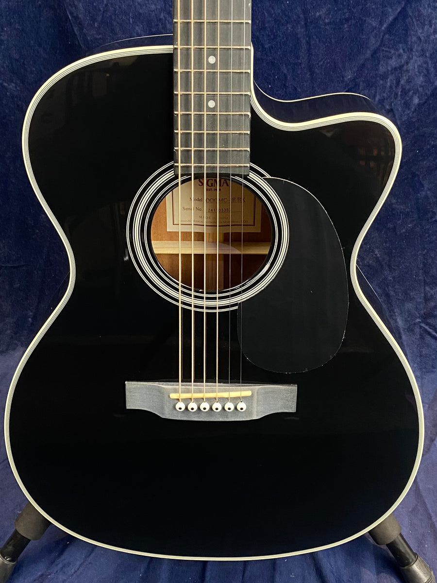 Glossy black acoustic guitar with a cutaway body, white trim along the edges, six strings, and a round sound hole with a visible label inside.
