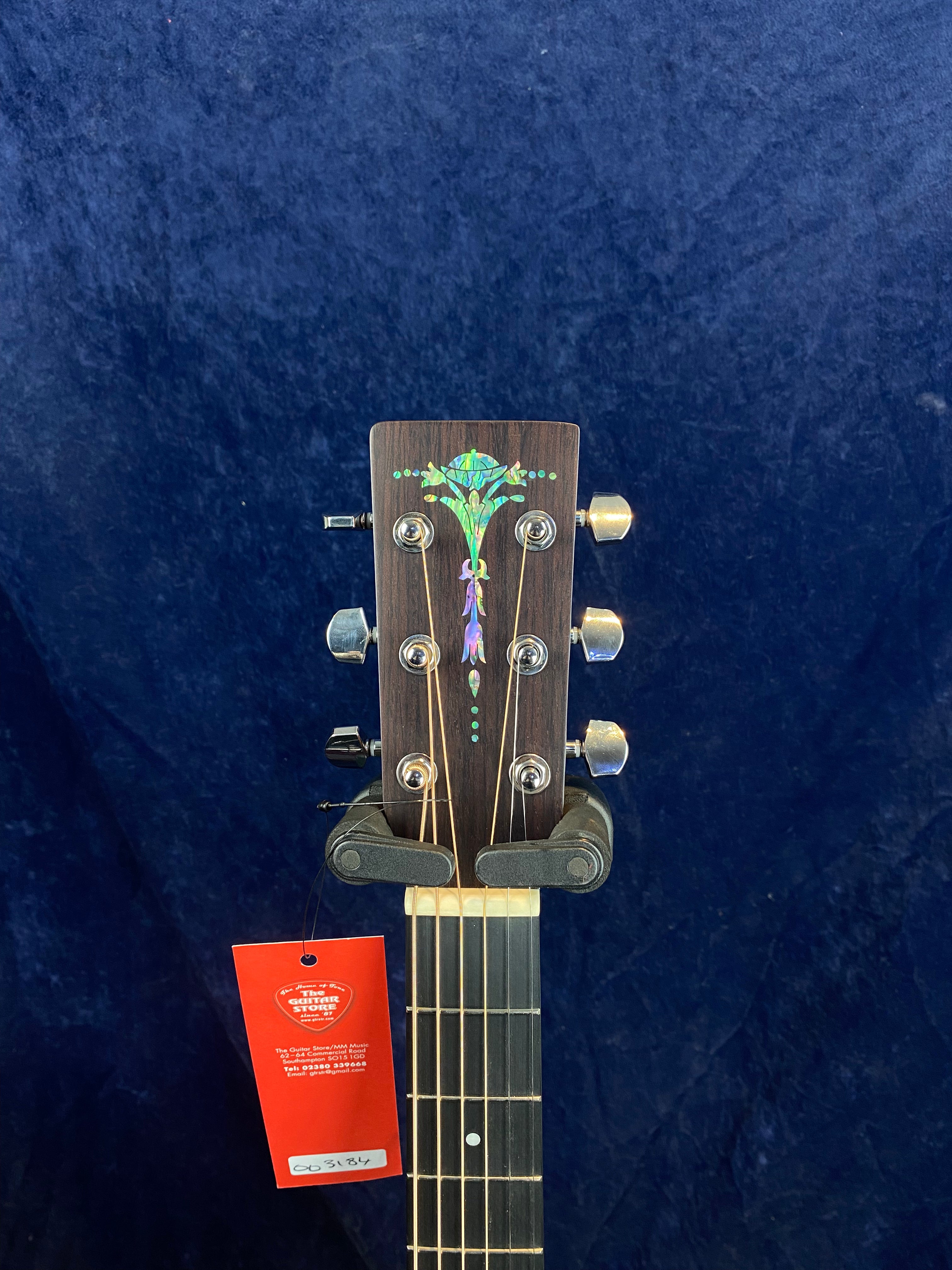 Acoustic guitar headstock with abalone floral inlay, six tuning pegs, and a red tag attached just below the nut.