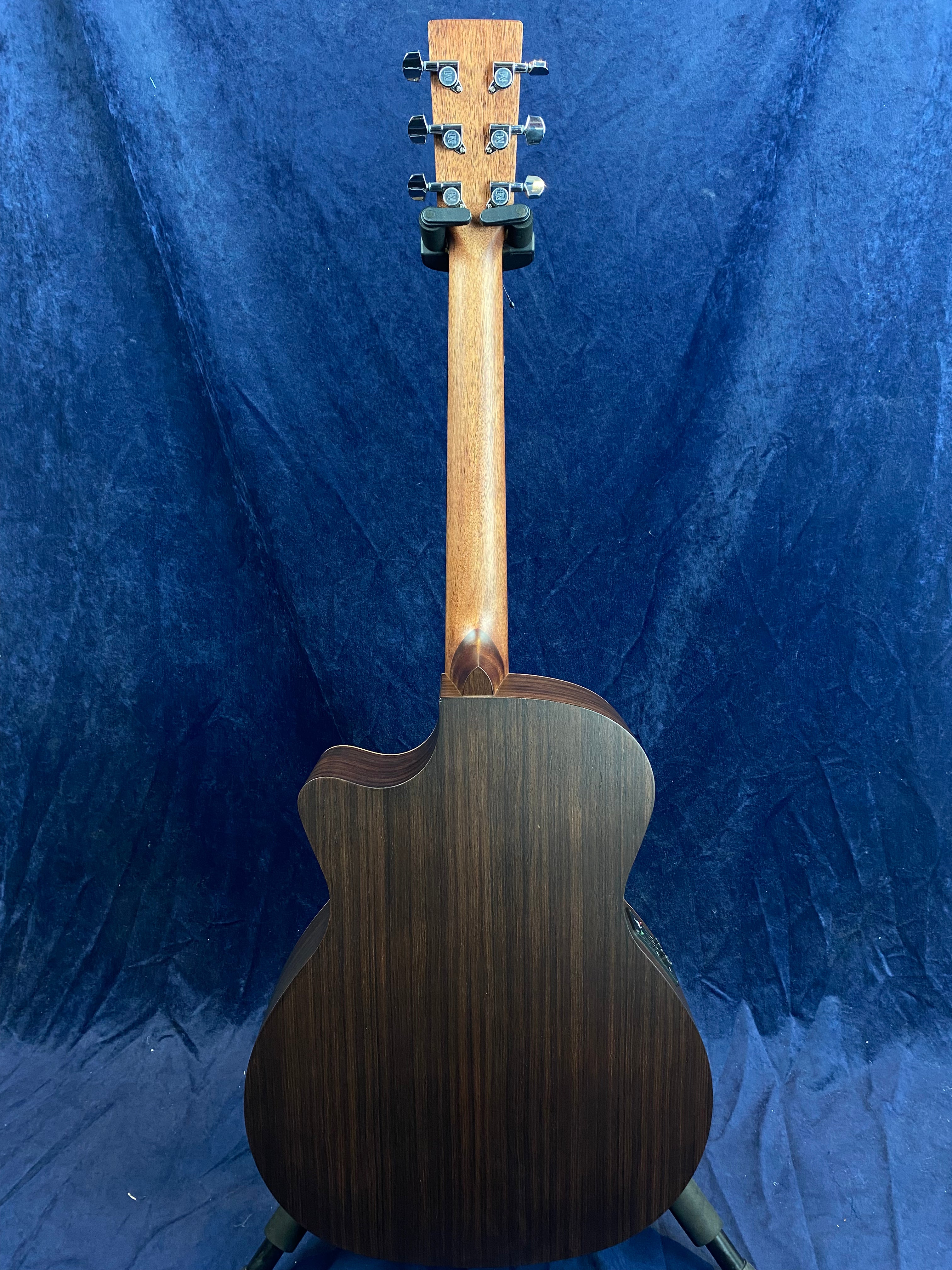 Dark wood acoustic guitar shown from the back, highlighting its smooth grain and single cutaway design, against a blue textured background.