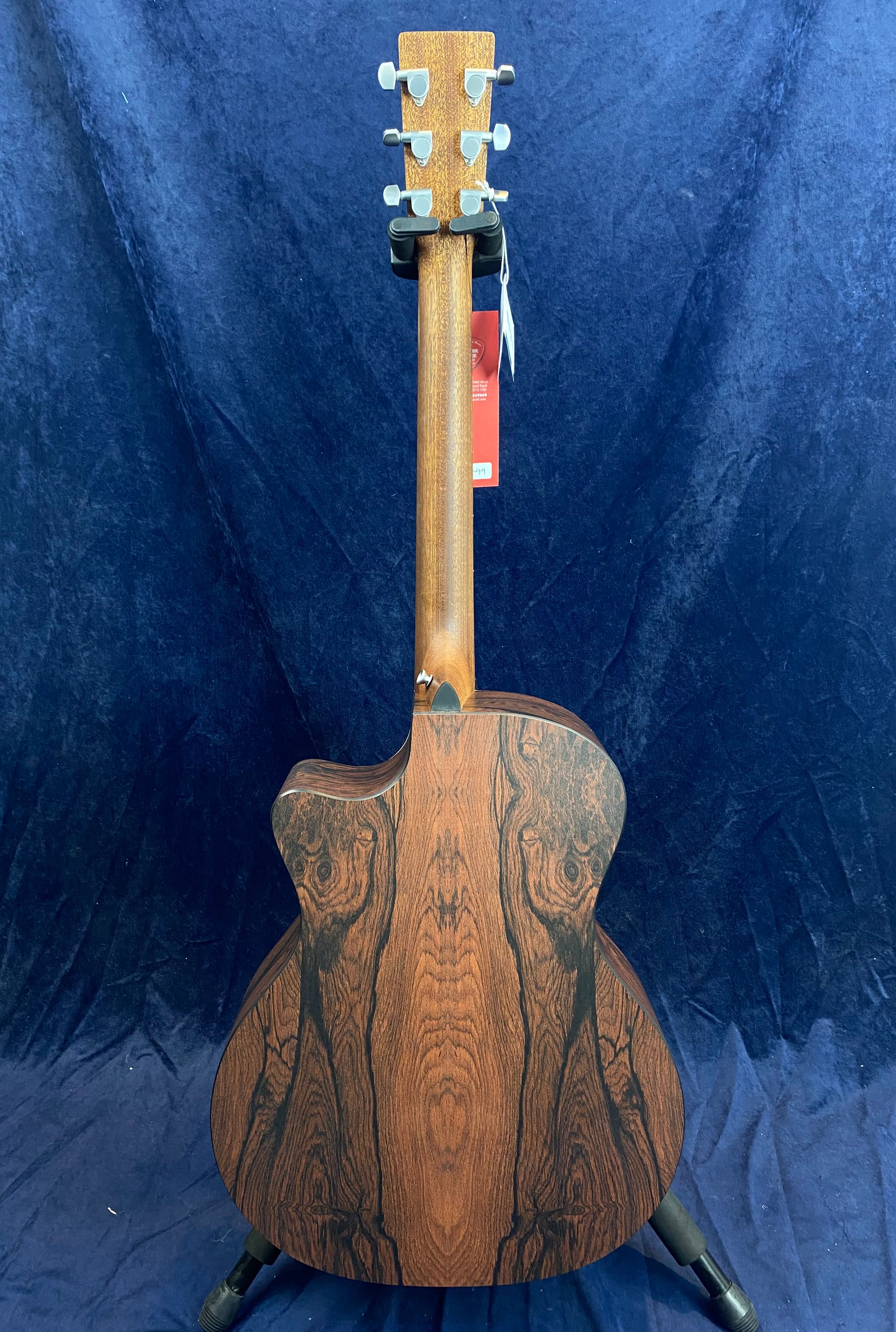 Acoustic guitar with a dark wood grain back and neck, featuring natural patterns and silver tuning pegs, shown from the rear against a blue background.