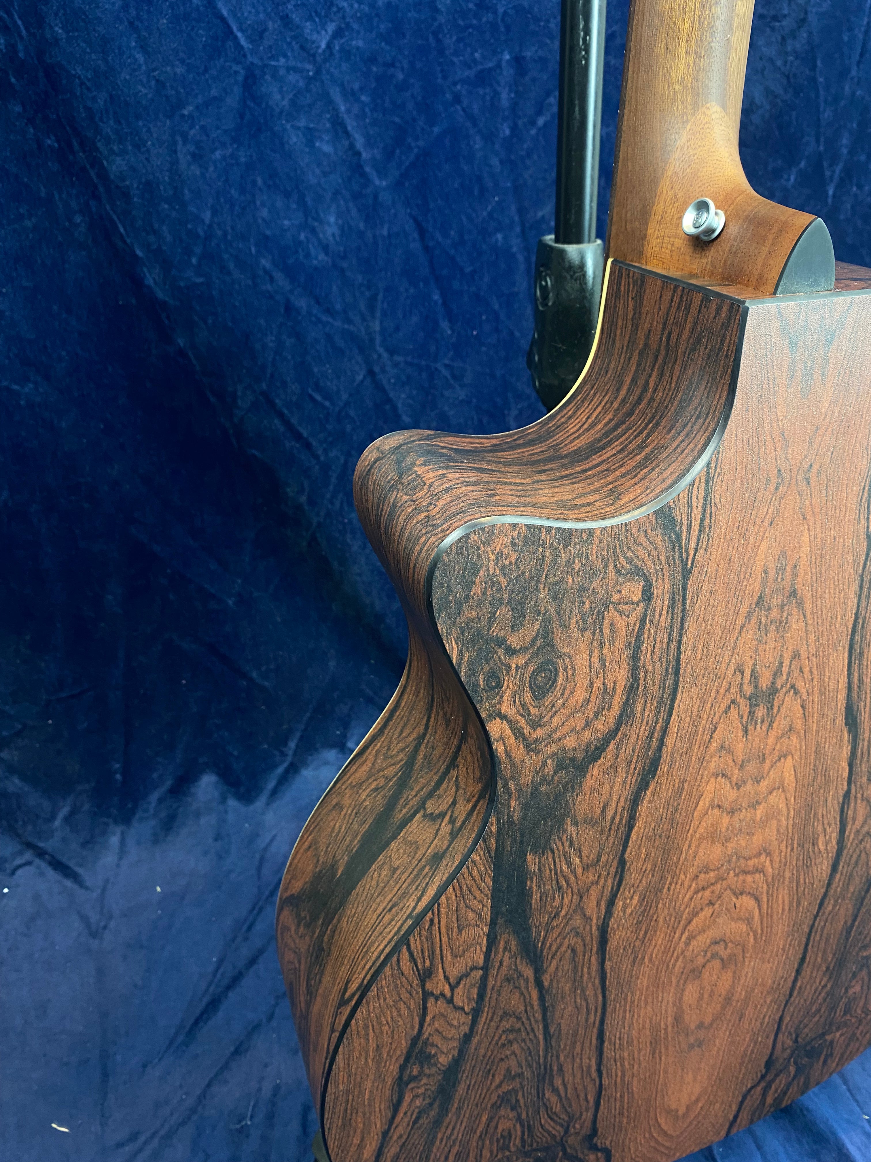 Acoustic guitar body with a natural dark wood grain finish and a smooth cutaway, resting against a dark blue textured background.