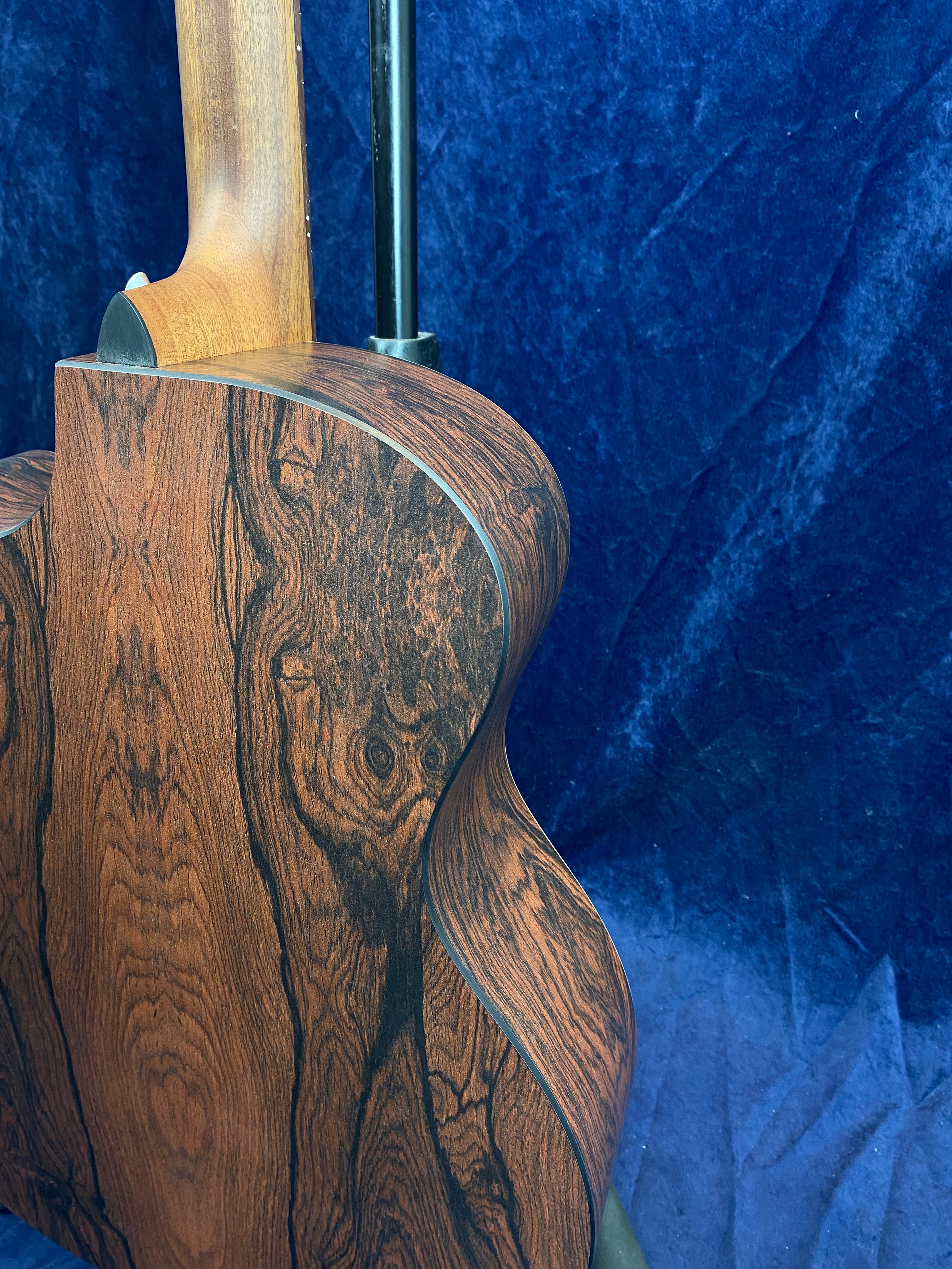 Acoustic guitar back and side with dark brown wood grain and a smooth curve, set against a textured deep blue background.
