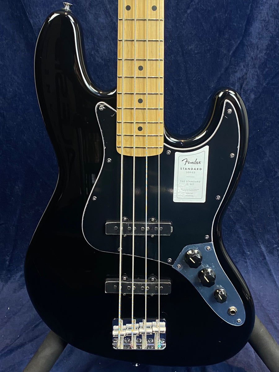 Glossy black Fender electric bass with a maple neck, chrome bridge, three control knobs, and a black pickguard against a dark blue background.