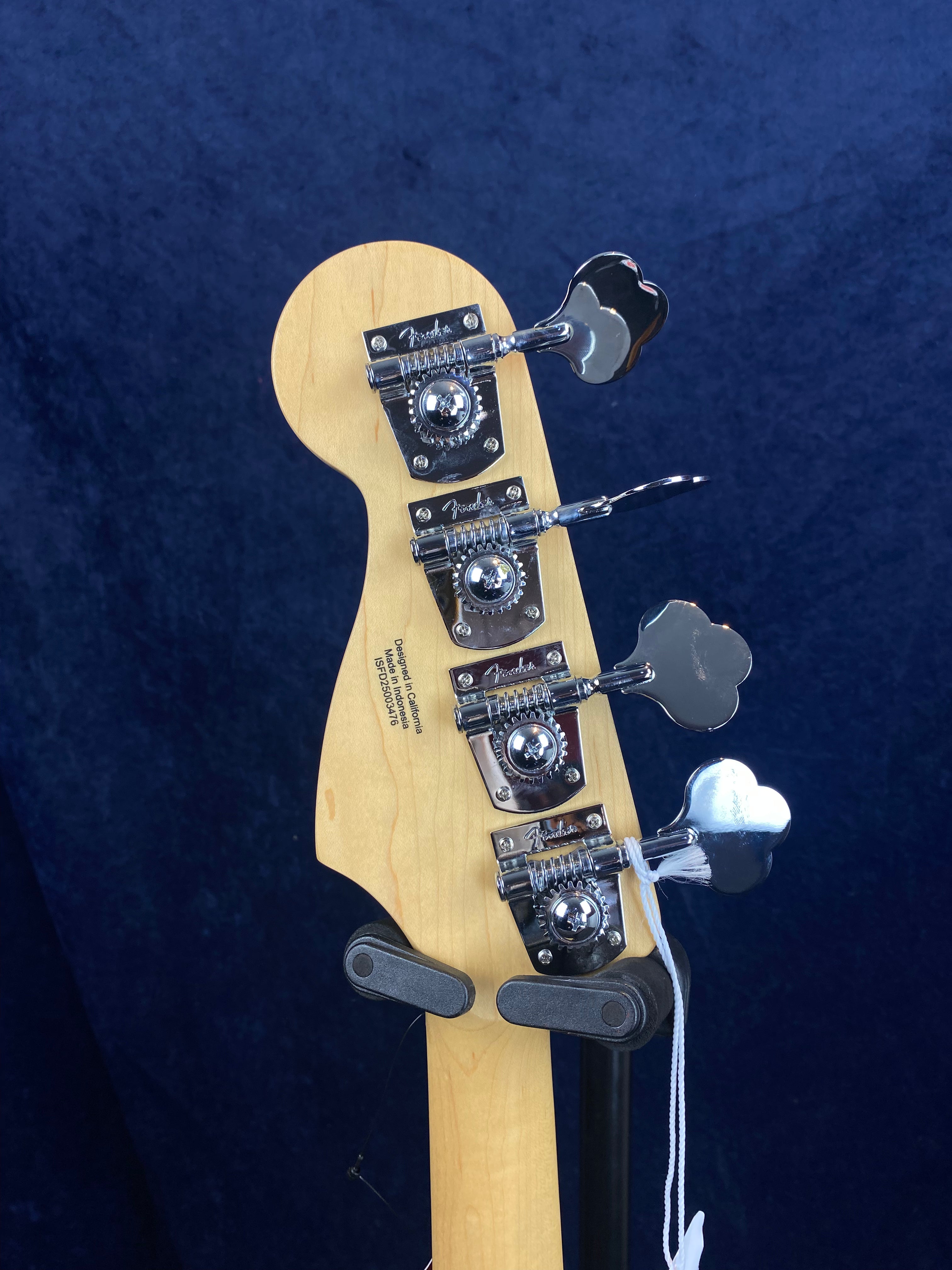The back of a Fender electric bass headstock shows four chrome tuning pegs against a dark blue background.