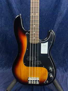 Sunburst Fender electric bass with four strings, black pickguard, two control knobs, and a sticker on the body above the pickups.