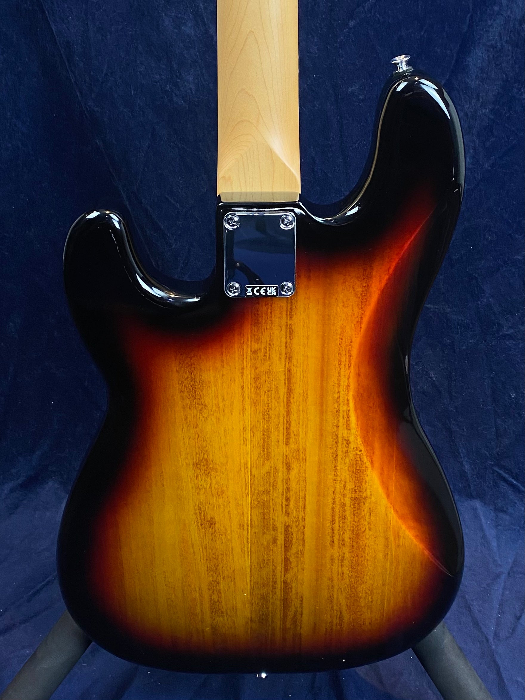 Electric bass guitar back showing sunburst wood finish, four-bolt neck plate, and natural maple neck, set against a dark background.