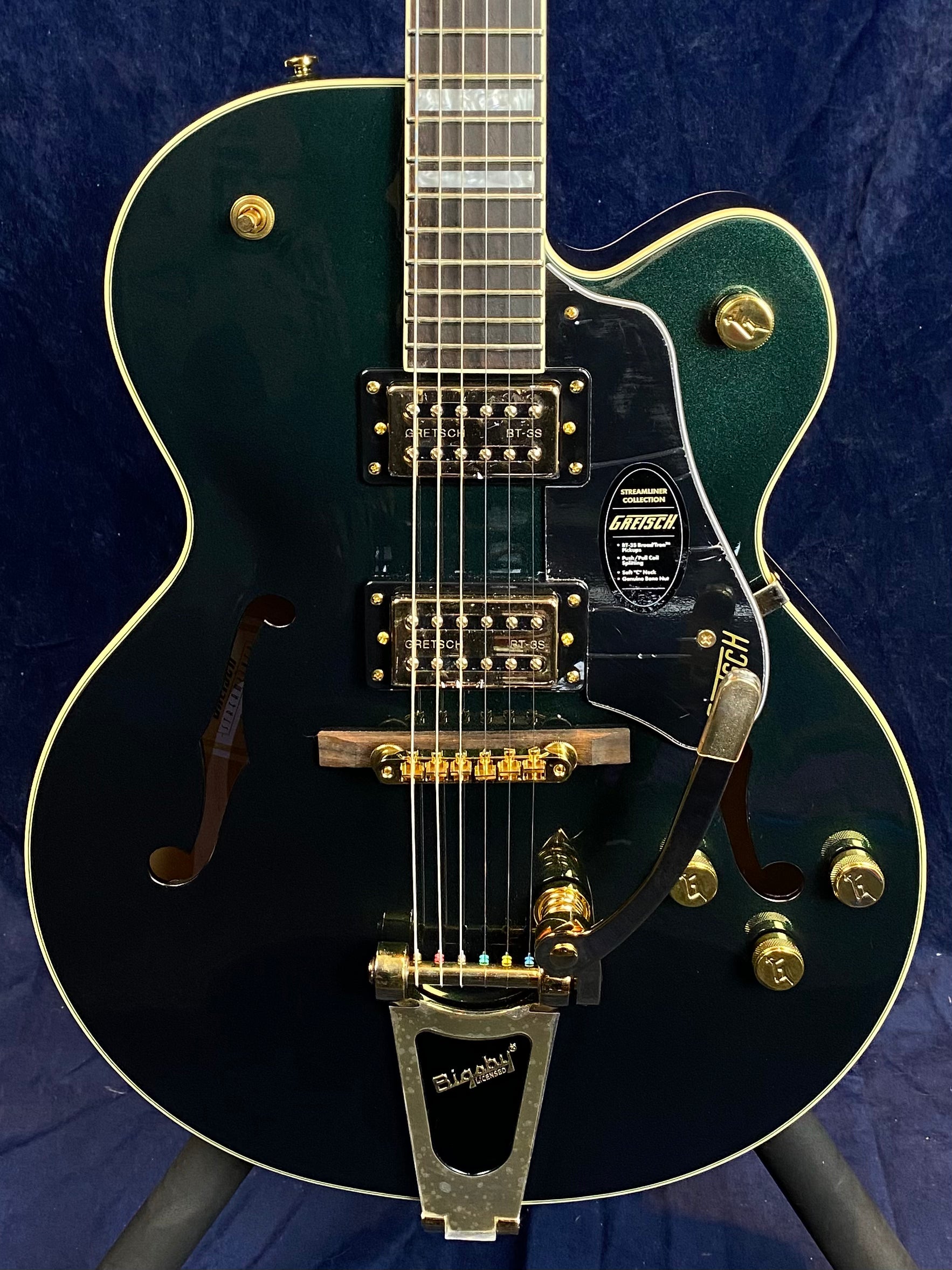 Dark green Gretsch electric guitar with gold hardware, two humbucker pickups, Bigsby tremolo, and f-holes on a hollow body.