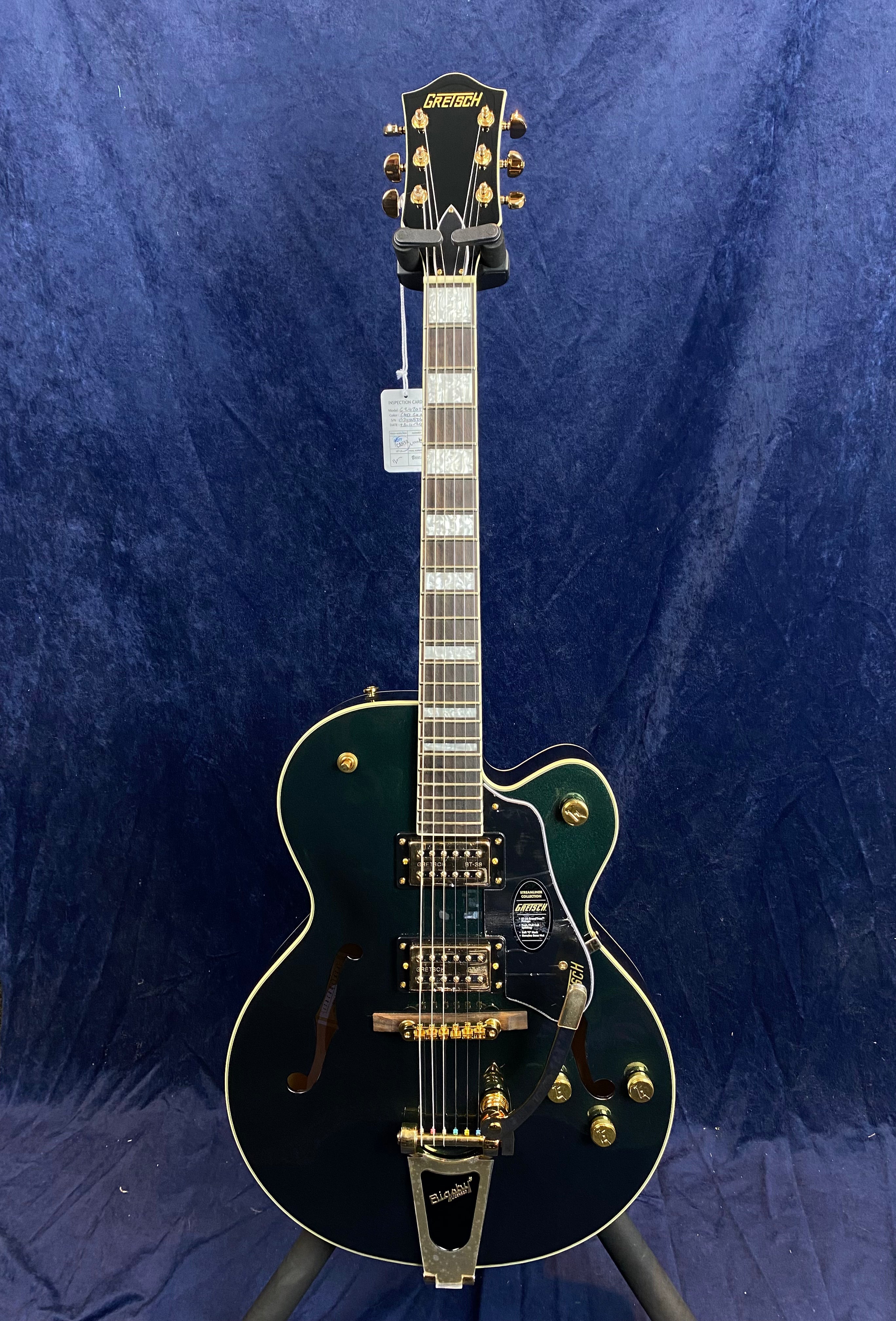 Gretsch electric guitar with dark green hollow body, gold hardware, two pickups, Bigsby tremolo, and pearloid block inlays on the fretboard.