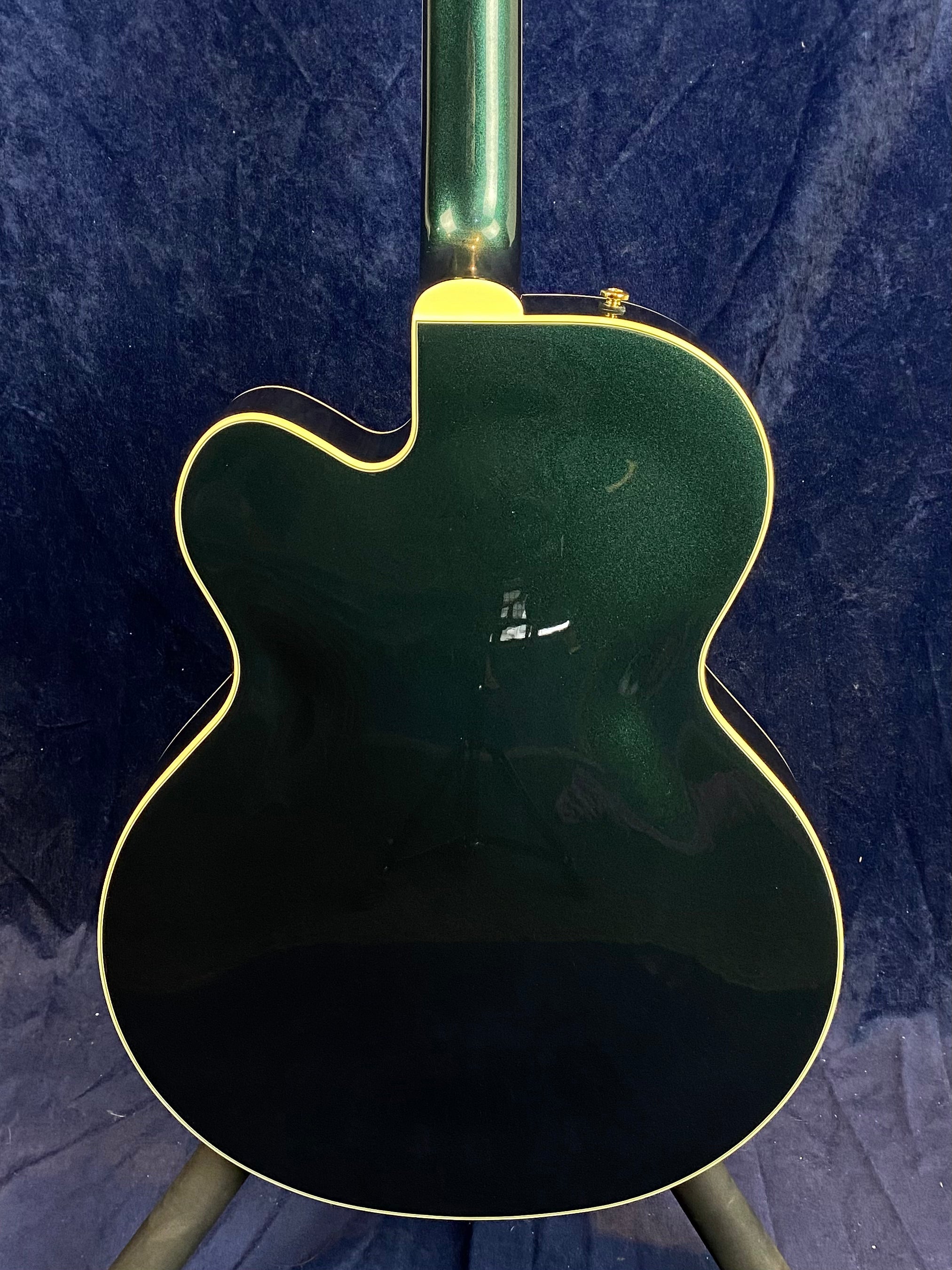 Green electric guitar with a single cutaway body, cream binding along the edges, shown from the back against a dark blue background.