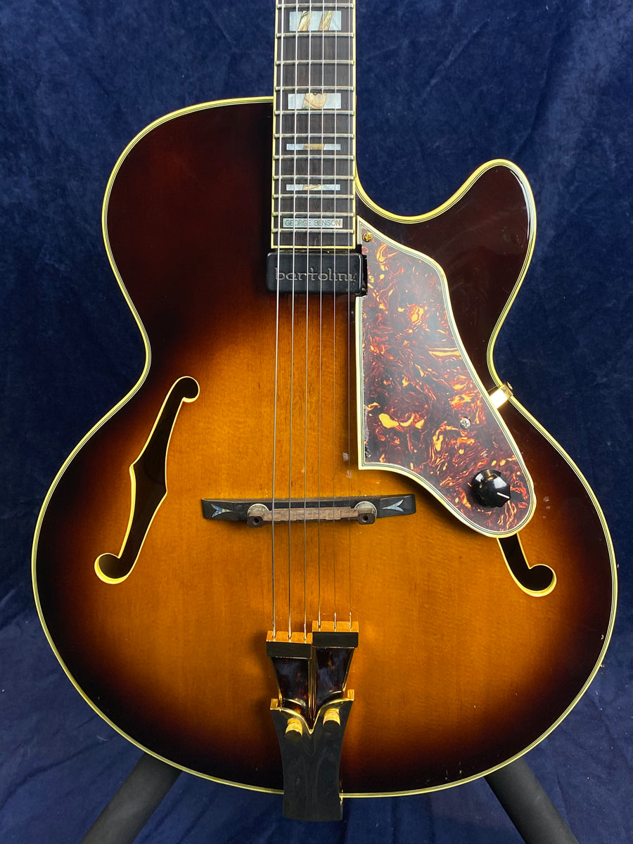 Sunburst archtop electric guitar with gold hardware, dark tortoiseshell pickguard, single neck pickup, and two f-shaped sound holes.