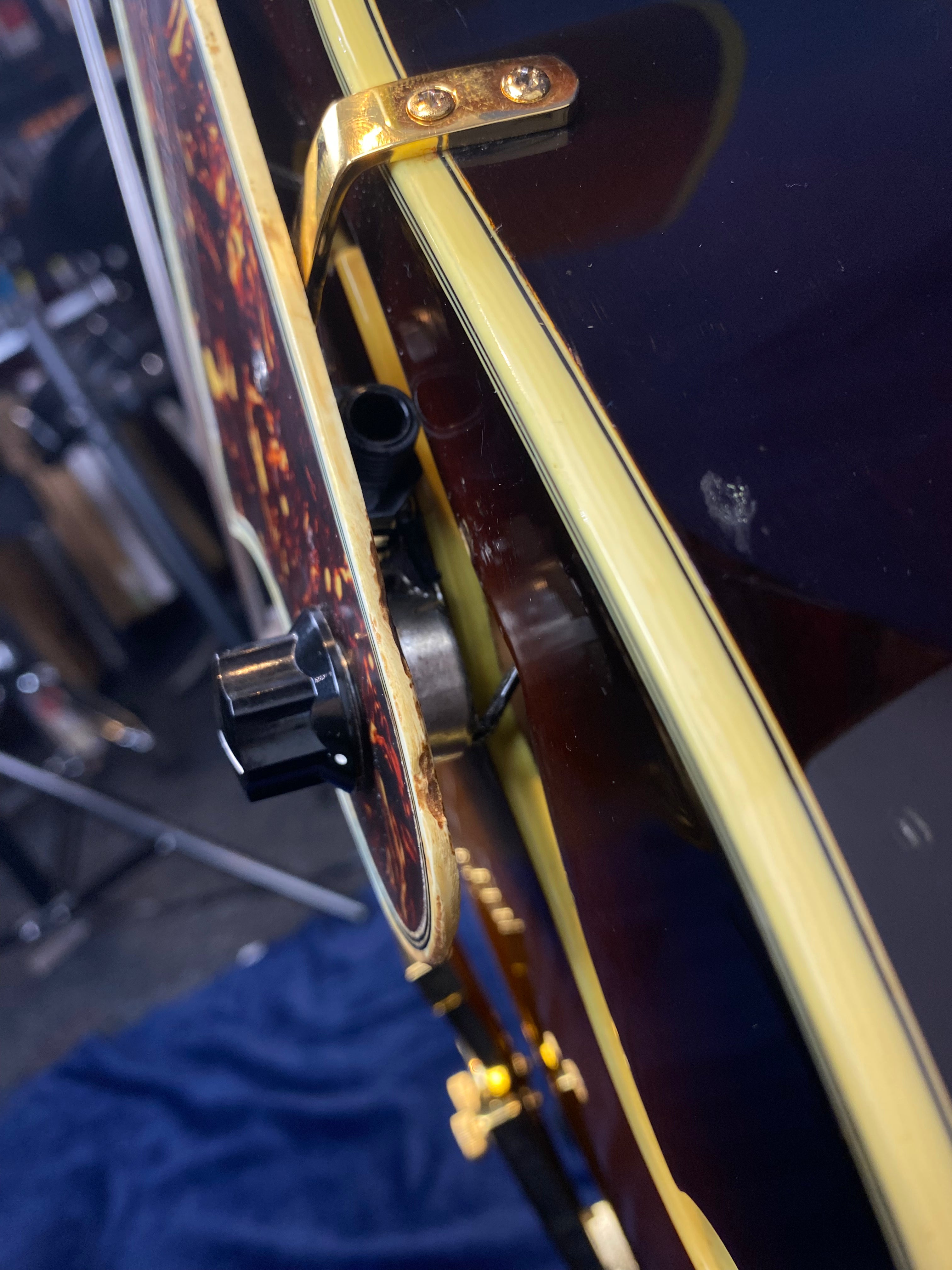 Close-up of a hollow-body electric guitar showing gold hardware, cream binding, a control knob, and an input jack on a dark, glossy body.