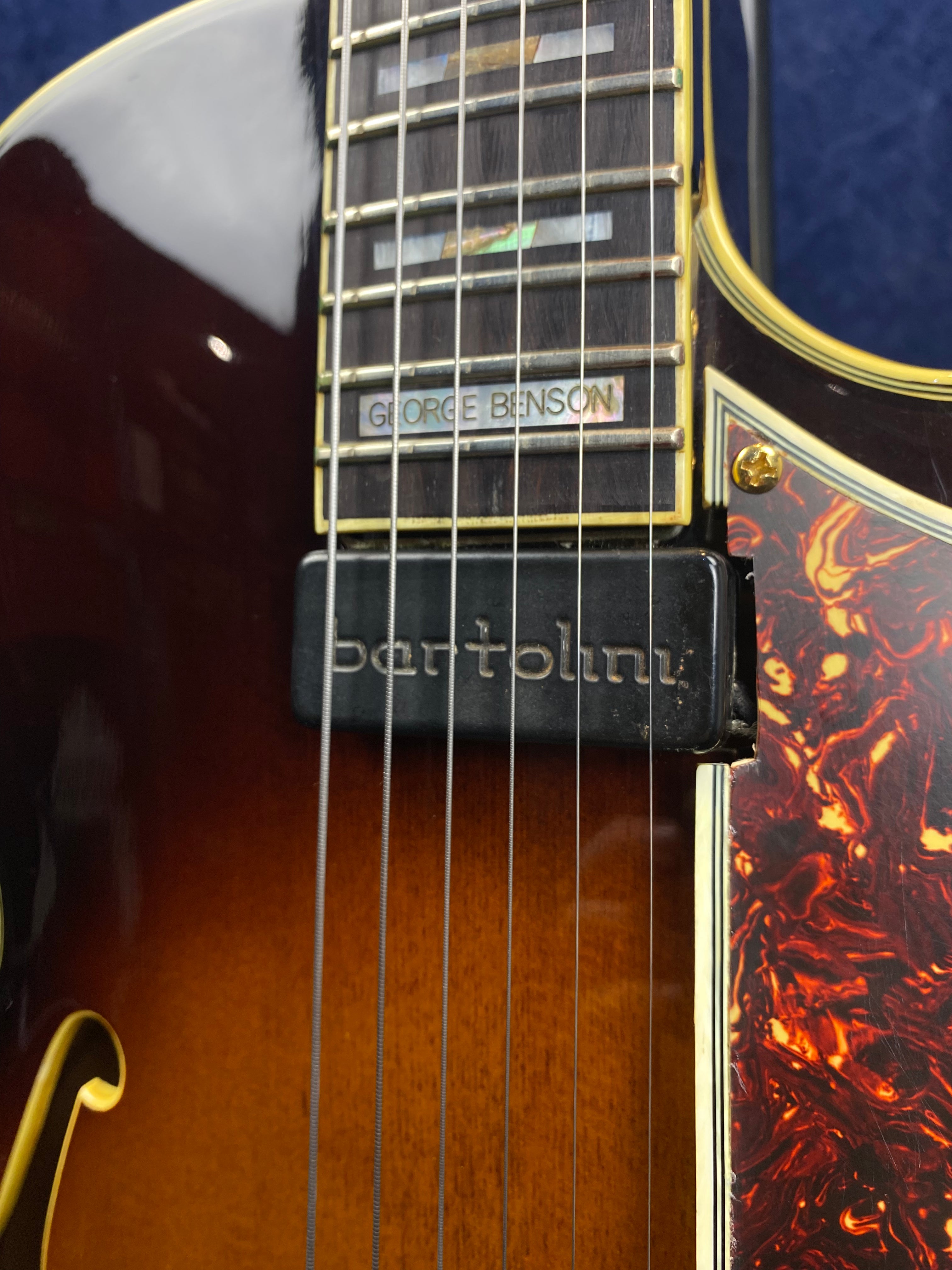 Close-up of an electric guitar showing a Bartolini pickup, "George Benson" inlay on the fretboard, and a tortoiseshell-patterned pickguard.