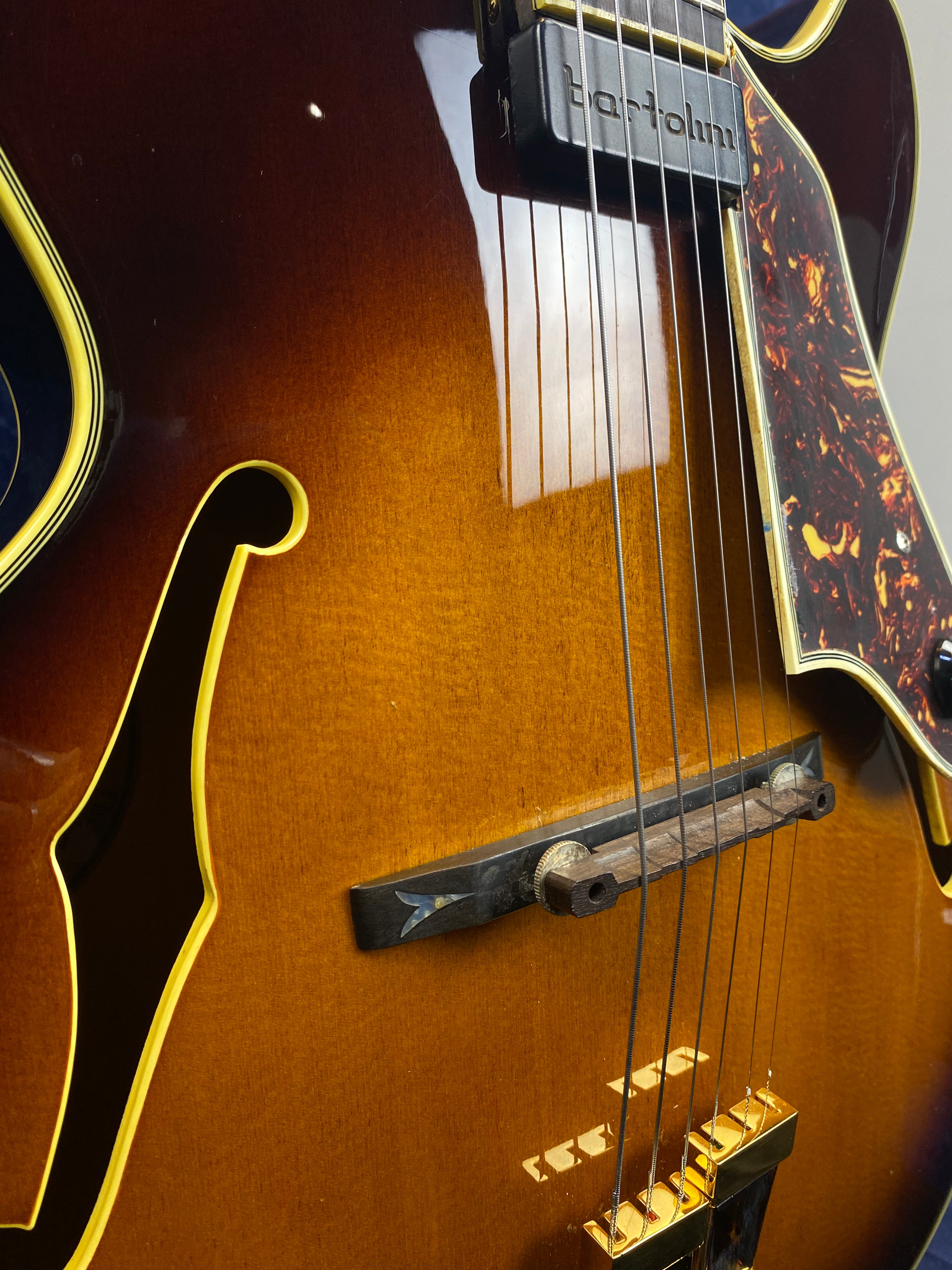 Close-up of a sunburst hollow-body electric guitar showing f-hole, floating bridge, tortoiseshell pickguard, and Bartolini pickup.