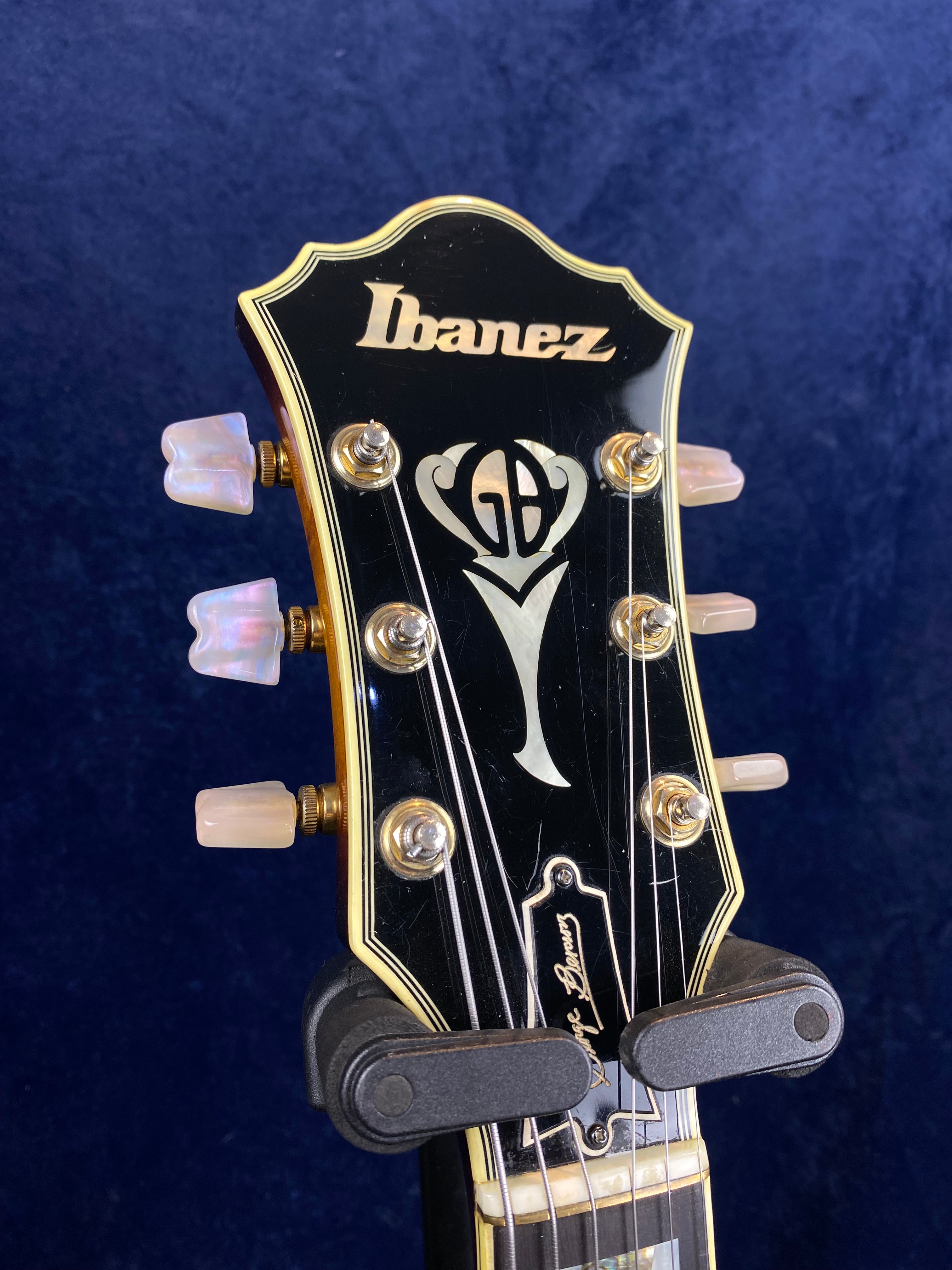 Ibanez electric guitar headstock with gold trim, pearl tuning pegs, and an inlaid "GB" logo design above the signature "George Benson."