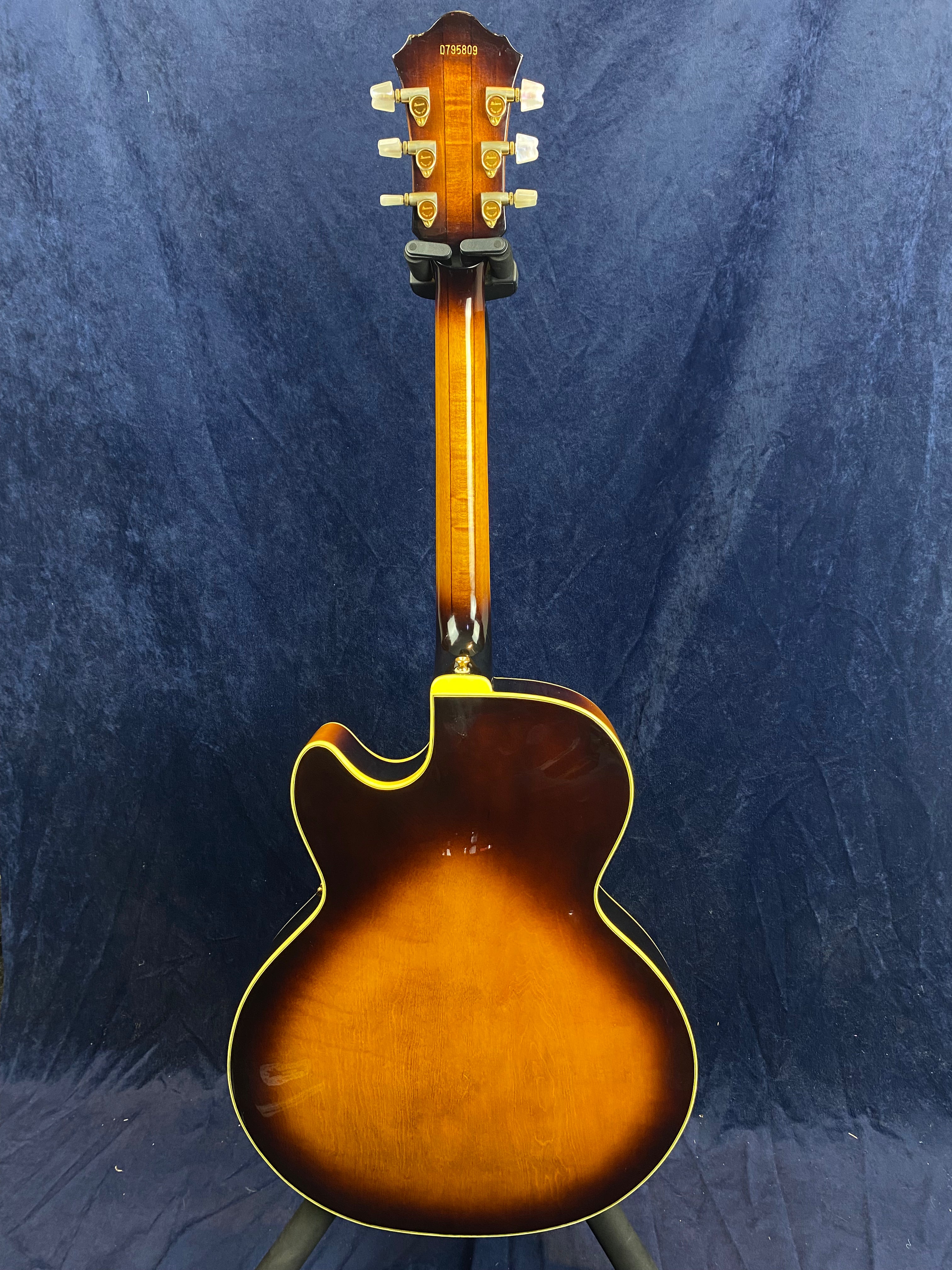 Sunburst-finish electric guitar shown from the back, single cutaway body, yellow binding, vintage-style tuners, visible serial number on headstock.