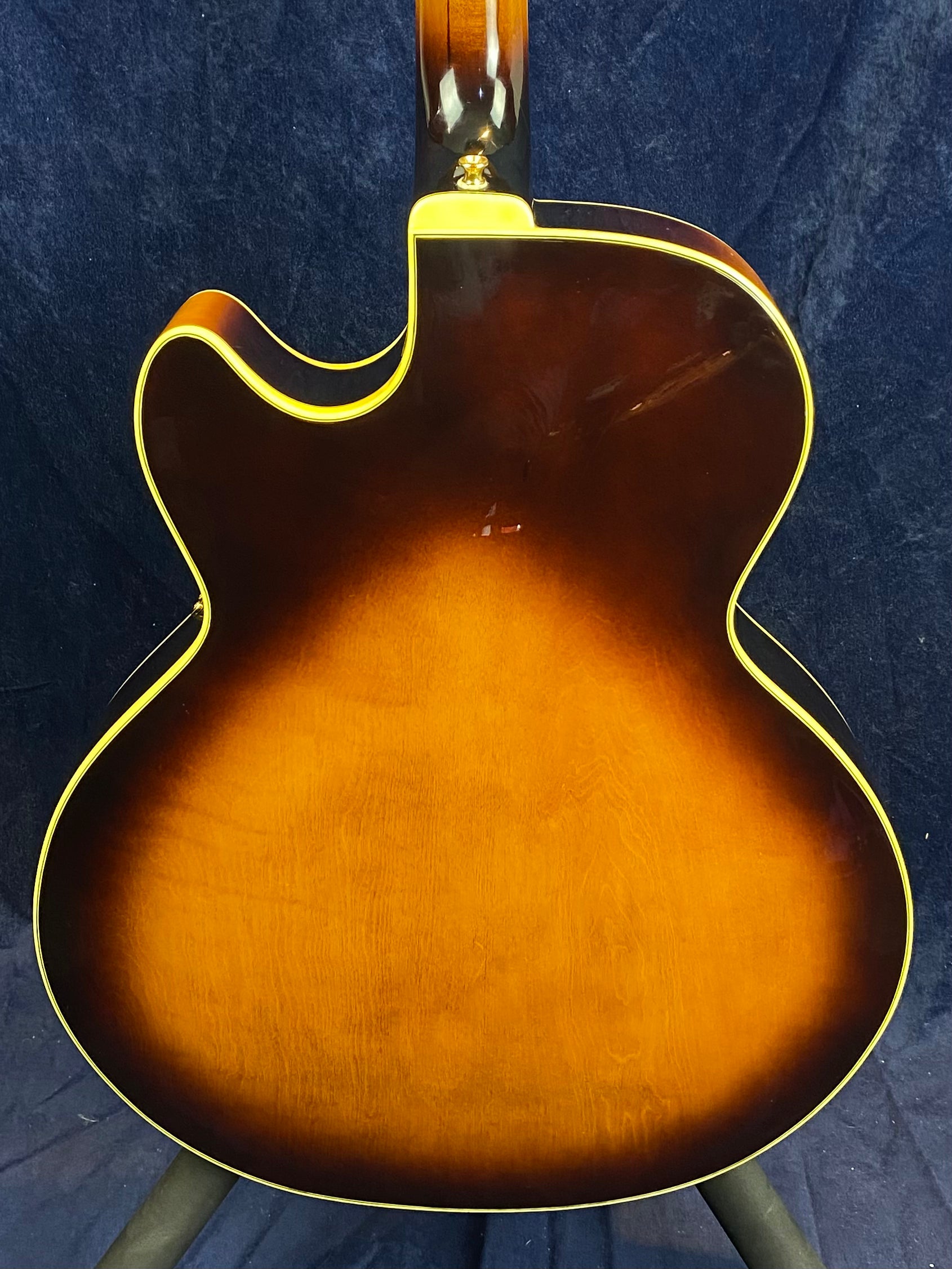 Archtop electric guitar with a sunburst finish, yellow trim, and a single cutaway on the upper body, viewed from the back against a dark background.