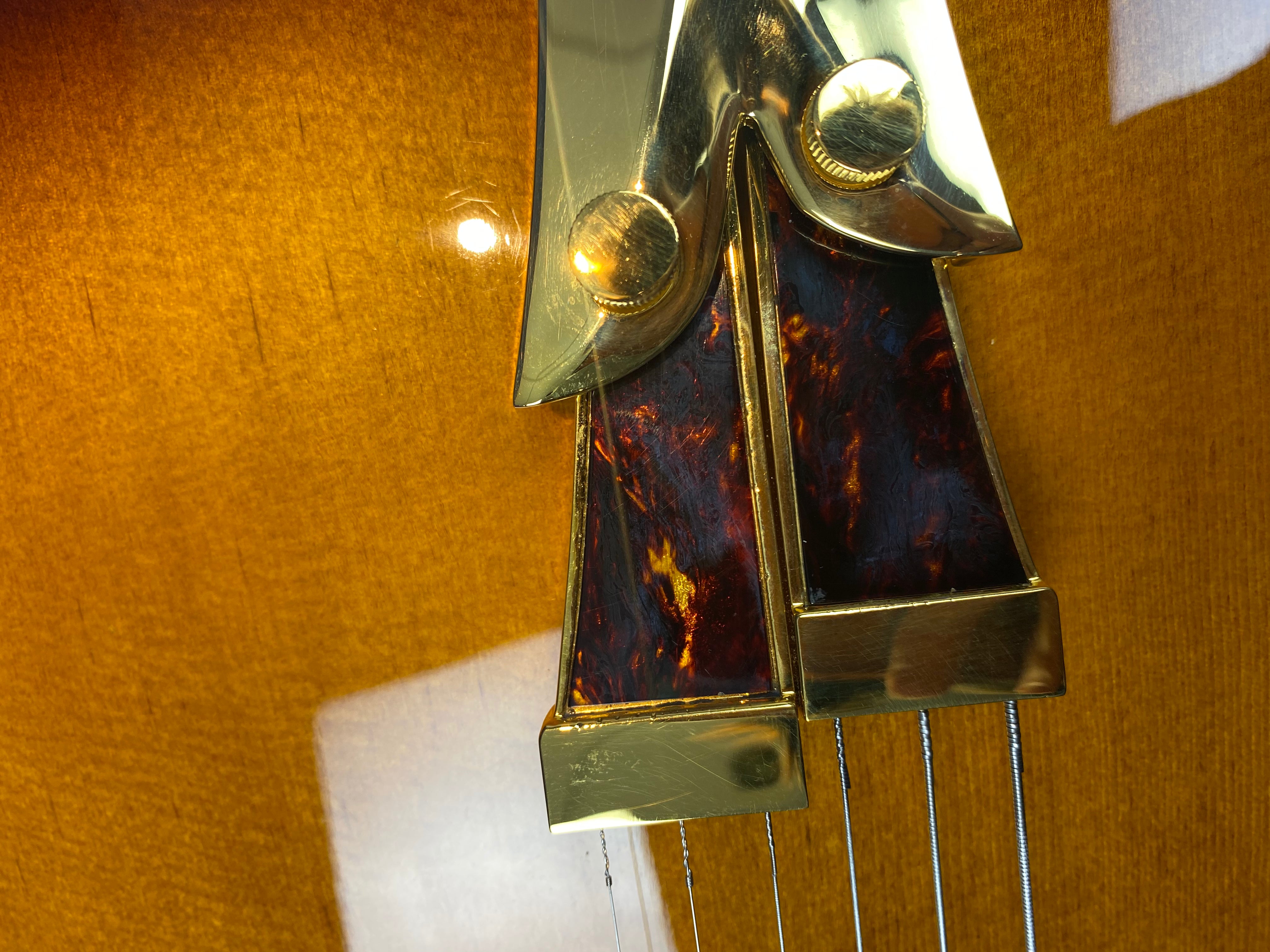 Close-up of an electric guitar tailpiece with gold metal, tortoiseshell accents, and visible strings against a glossy amber wood finish.