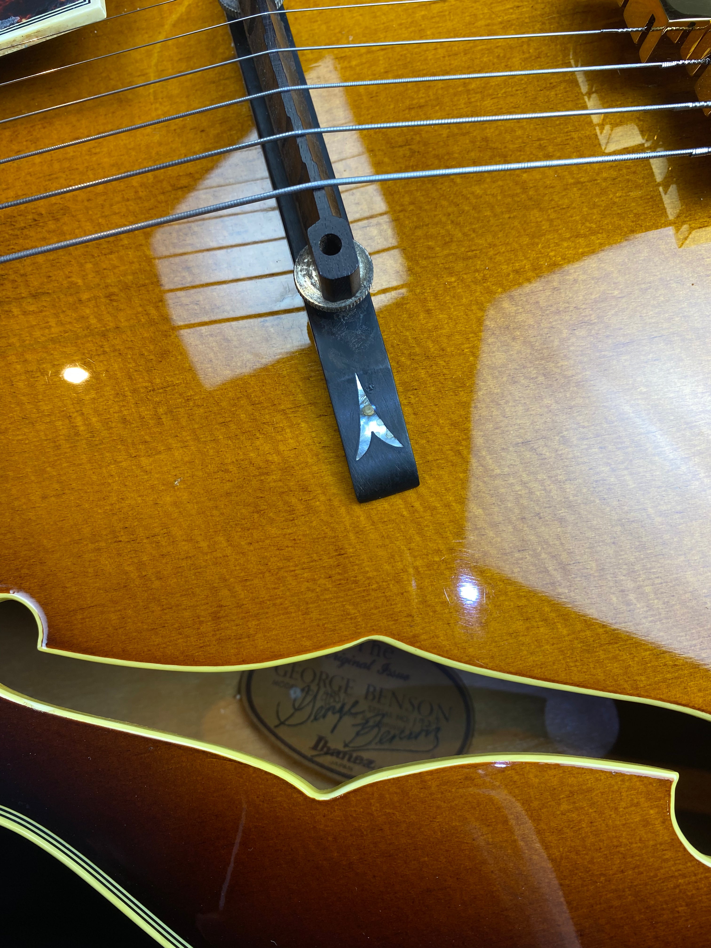 Glossy brown Ibanez electric guitar body with strings, wooden bridge, and a label inside the f-hole reading "George Benson."