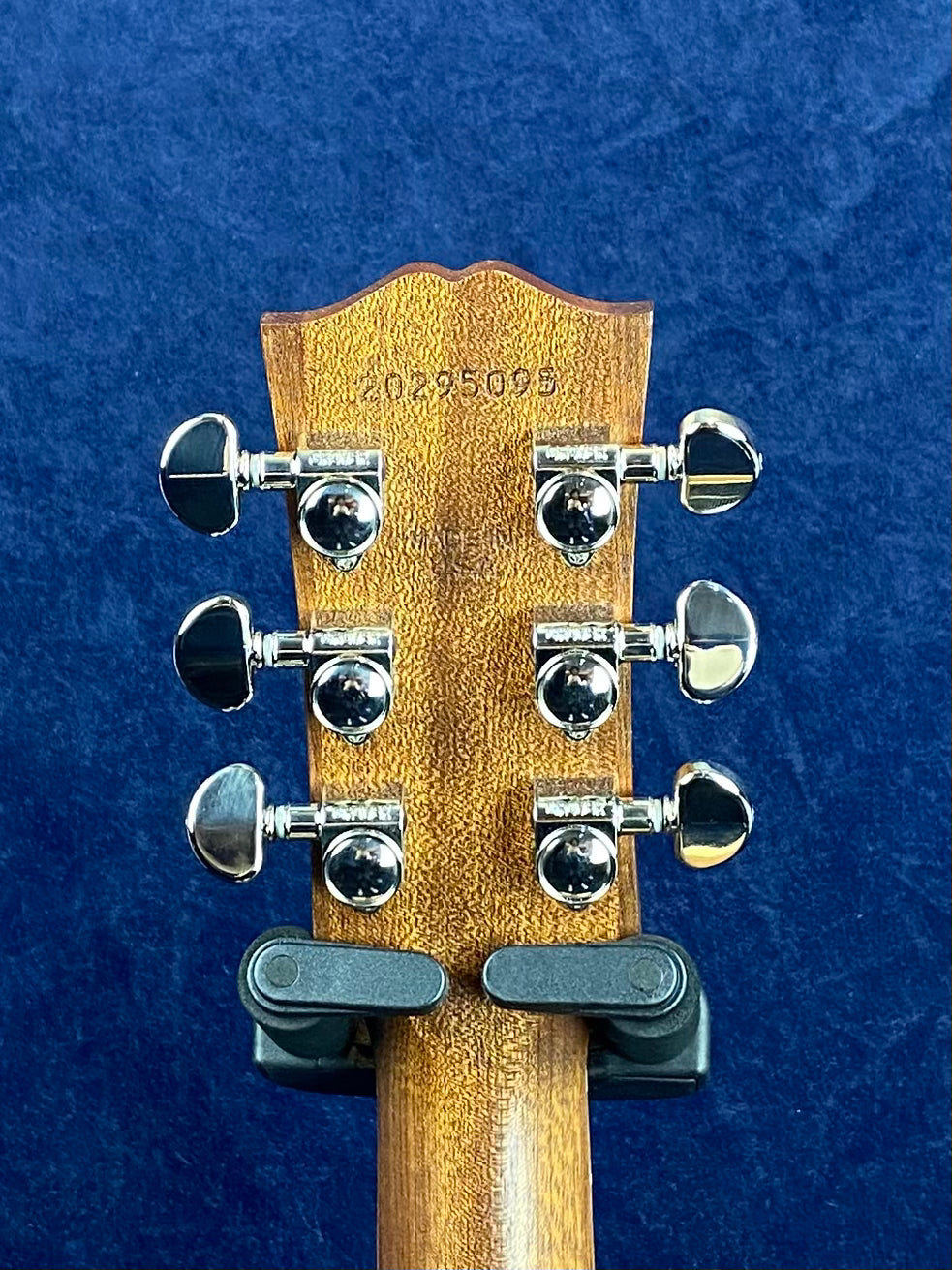 Six chrome tuning pegs on the back of a wooden acoustic guitar headstock; the serial number 20295098 is stamped at the top.