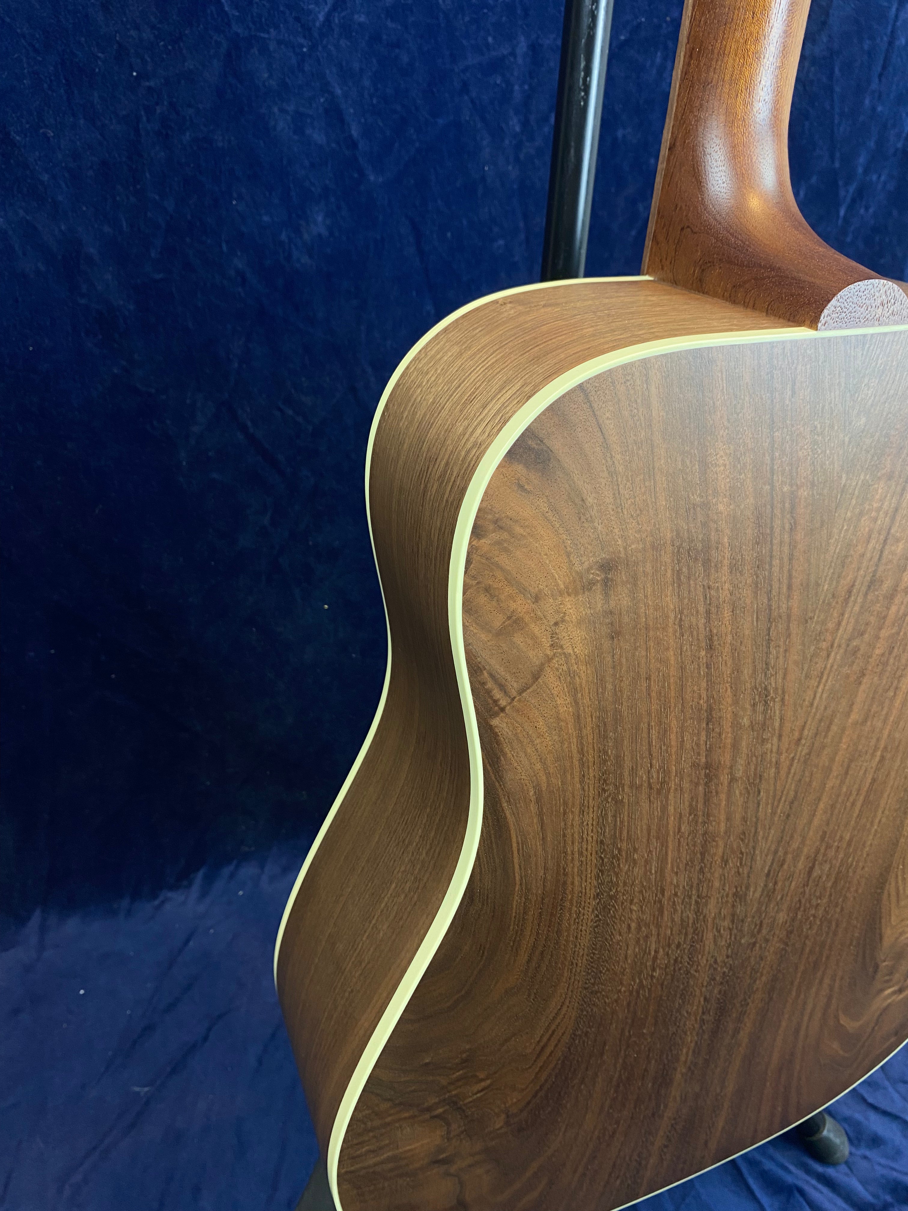 Curved back and side of an acoustic guitar with dark wood grain and cream binding, set against a dark blue background.