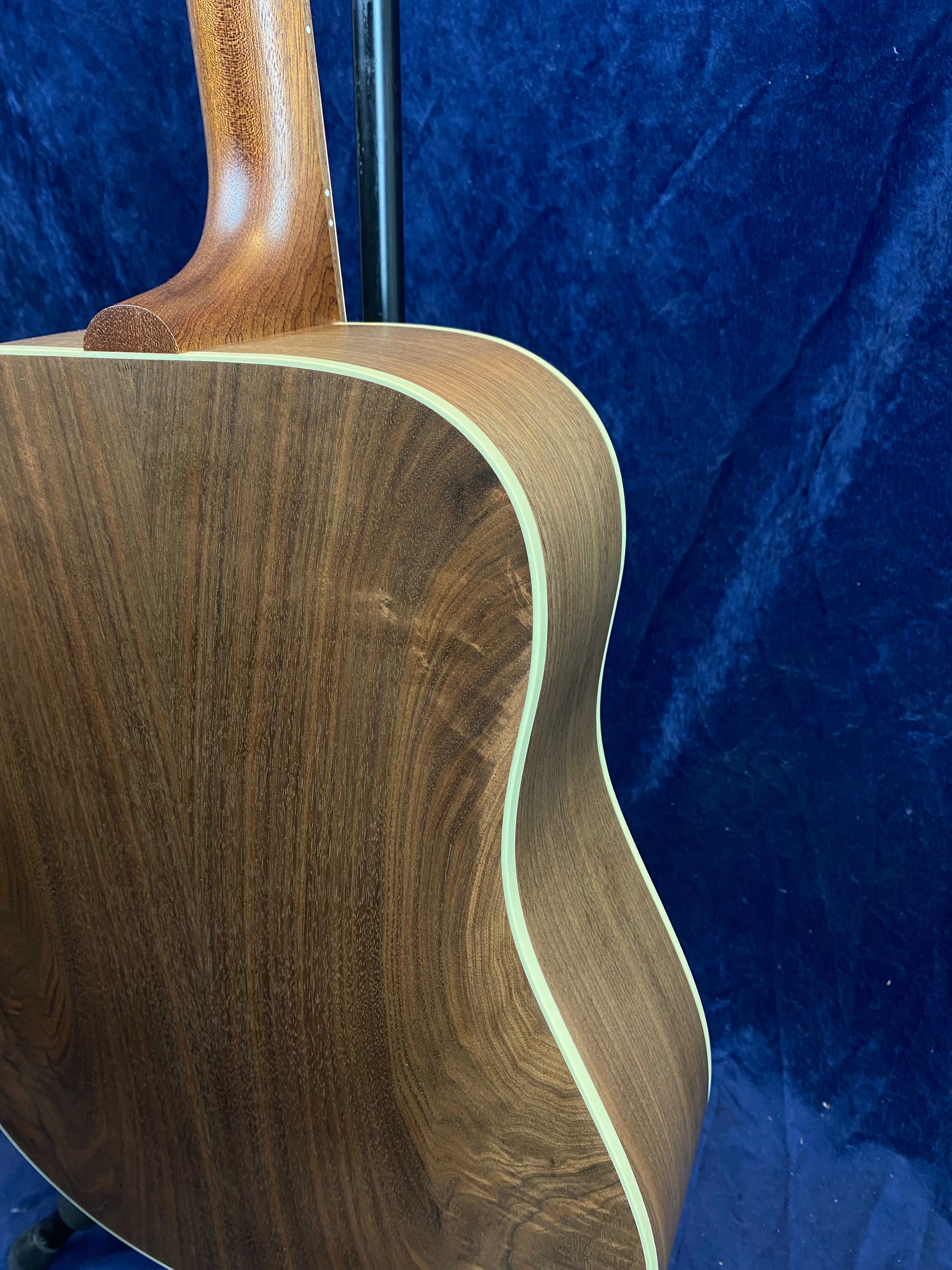 Acoustic guitar back and sides in smooth brown wood with light cream binding, shown against a dark blue textured background.