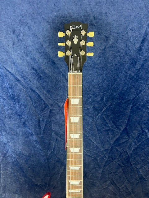 Gibson electric guitar headstock with six tuning pegs, mother-of-pearl inlays on the neck, and a red tag hanging from one of the tuning posts.