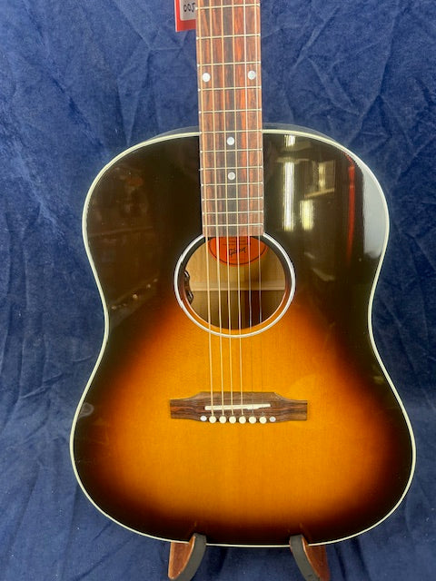 Acoustic guitar with a sunburst finish, white binding around the body, rosewood bridge, and visible steel strings against a dark blue background.