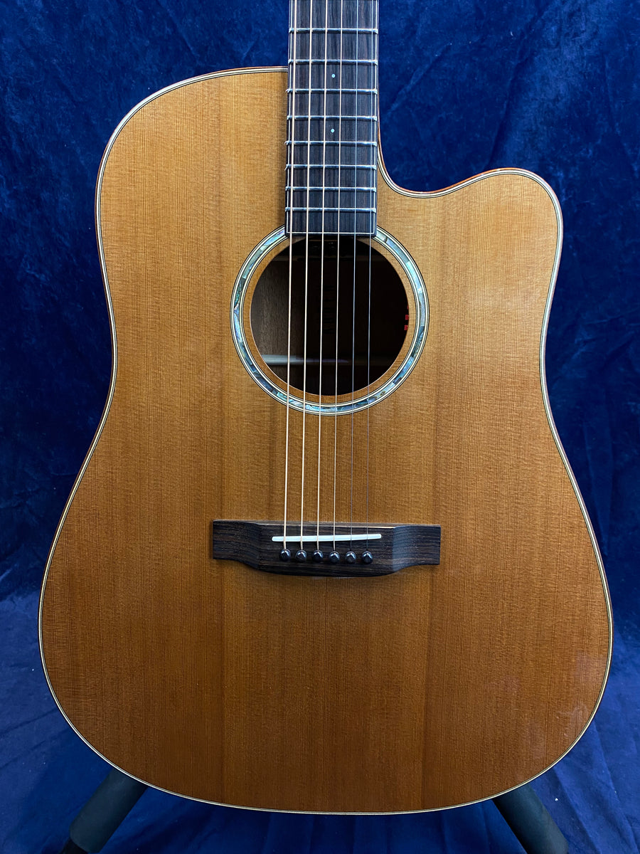 Natural wood finish acoustic guitar with six strings, a round sound hole, and a cutaway body design for easier access to higher frets.
