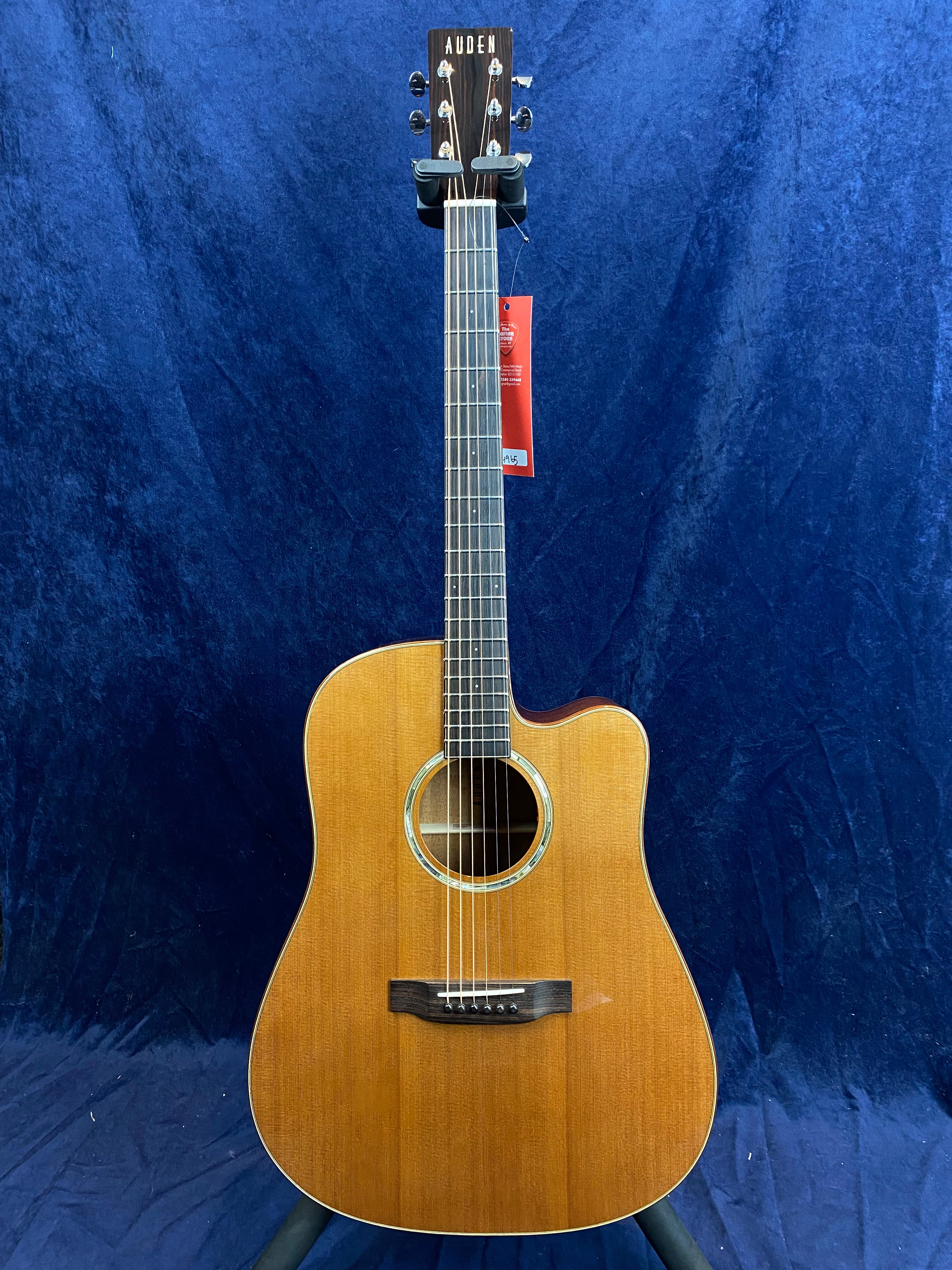 Auden acoustic guitar with a cutaway body, natural wood finish, six strings, and a circular sound hole, set against a dark blue background.
